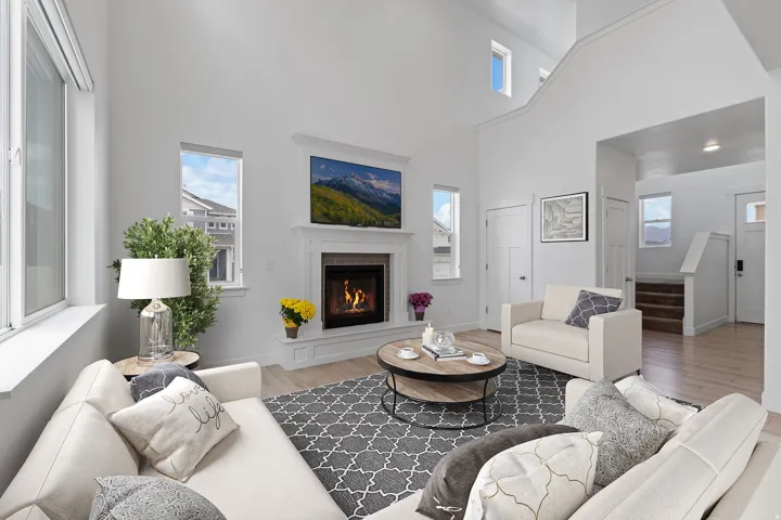 Vaulted ceiling living area featuring a fireplace with decorative mantel, multiple windows, and light wood-finish flooring