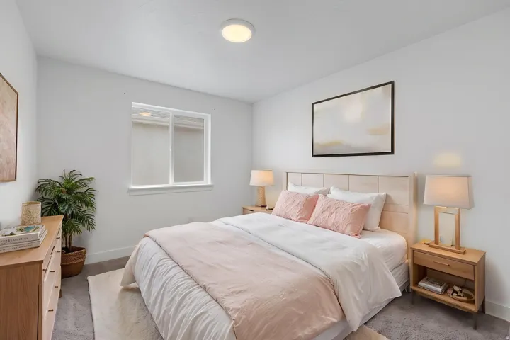 Bedroom featuring a light wood-finish headboard and frame, a window with white trim, a flush-mount ceiling light, and gray carpet flooring
