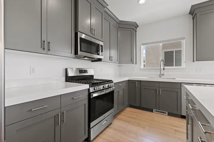 Modern kitchen featuring gray shaker-style cabinetry, stainless steel appliances, white countertops, a stainless steel sink with a gooseneck faucet, and wood-finish flooring