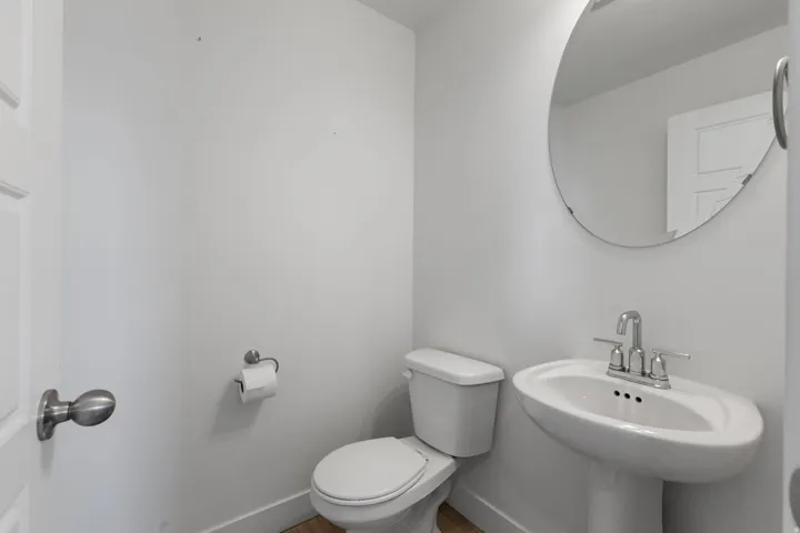 Pedestal sink with chrome faucet, circular mirror, and wood-finish flooring