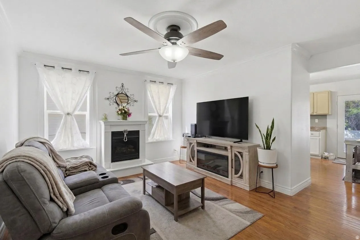 Living area featuring wood-finish flooring, a ceiling fan with integrated lighting, and a white mantel fireplace with an electric insert