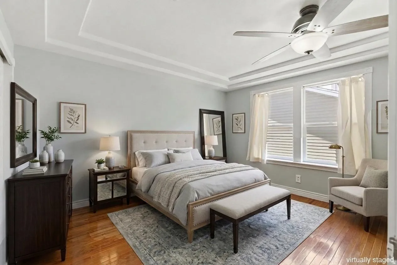 Recessed tray ceiling with crown molding, hardwood flooring, and a ceiling fan
