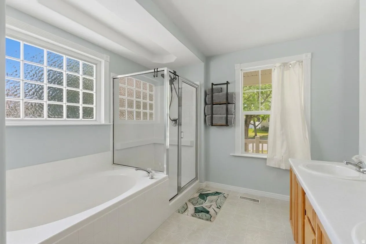 Bathroom featuring a built-in tub, separate glass-enclosed shower, glass block window, and a single vanity with wood-finish cabinetry