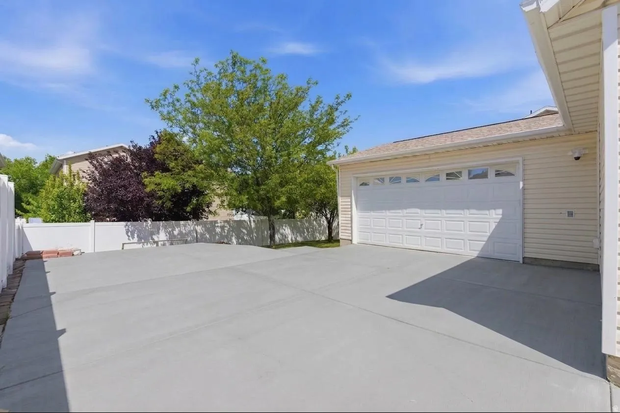 Spacious concrete driveway offering ample parking, featuring a two-car garage with panel-style doors and upper window inserts