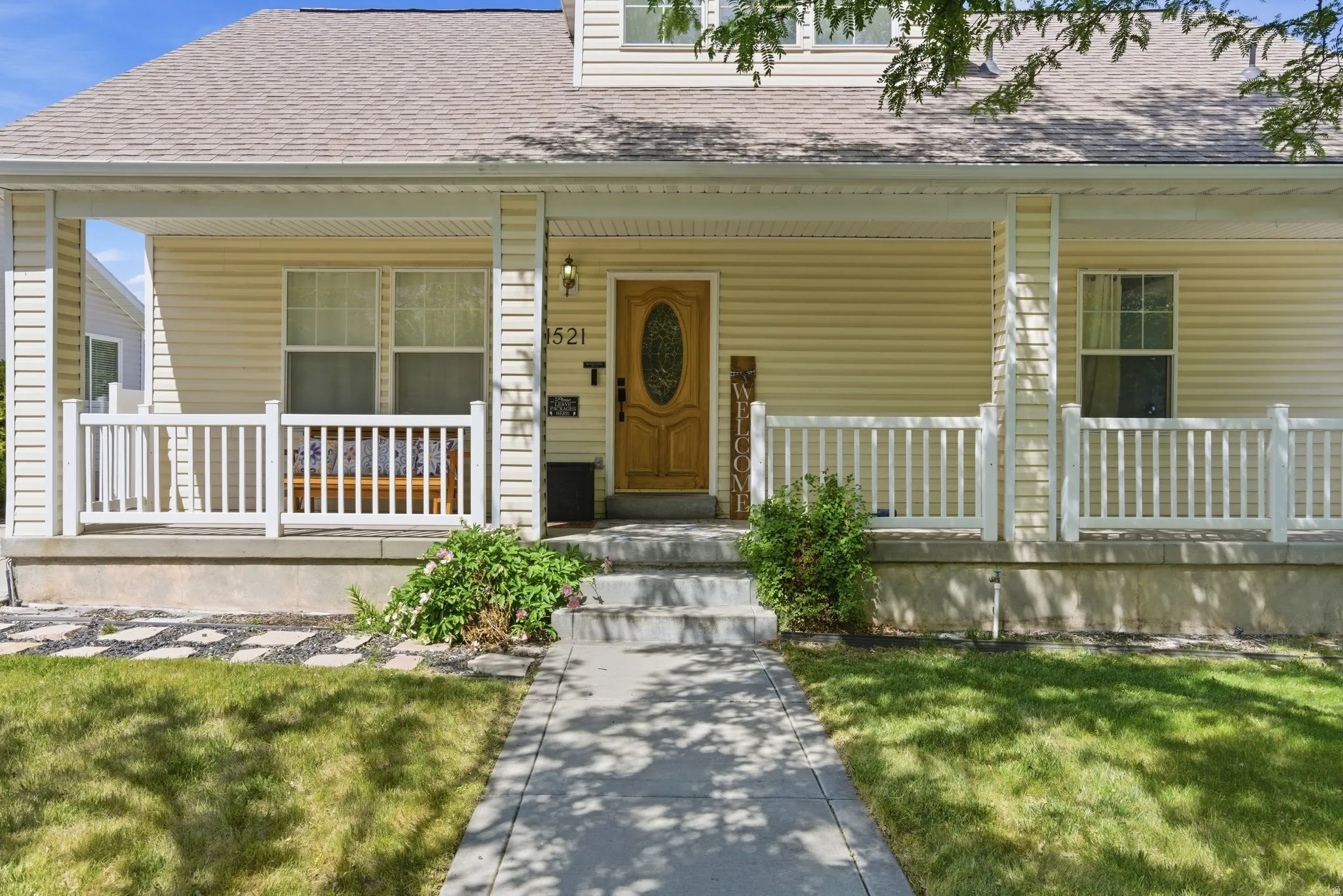 Inviting covered porch with white railing, light-toned siding, and a wooden entry door