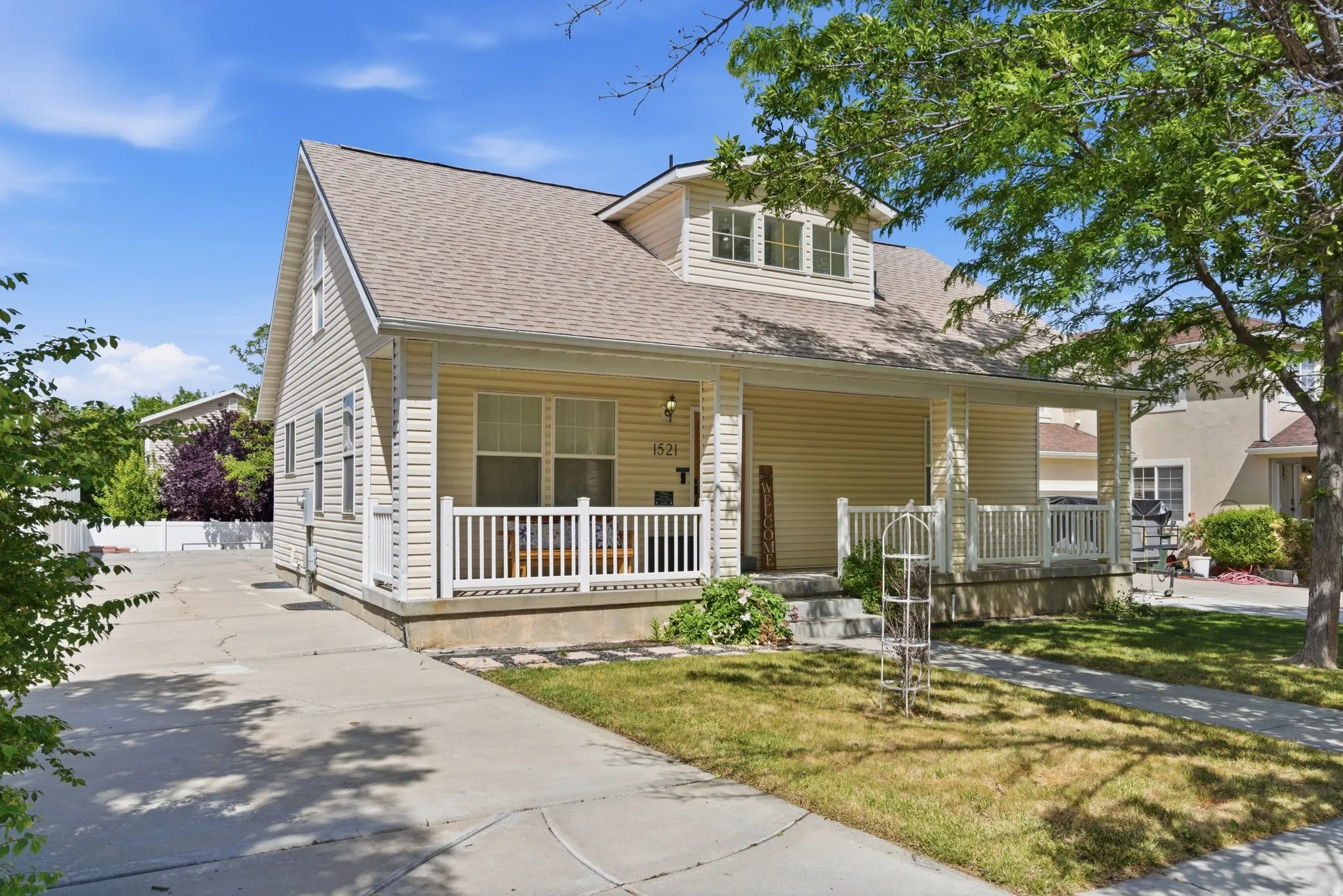 Exterior featuring light-toned siding, a covered porch with white railings, a multi-pane window dormer, a pitched roof, and a concrete driveway