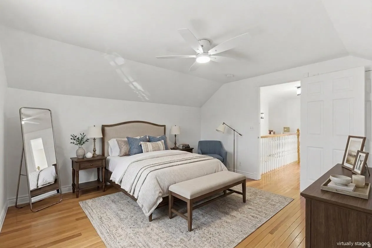 Hardwood flooring extends throughout this room, featuring a sloped ceiling and a ceiling fan with integrated lighting