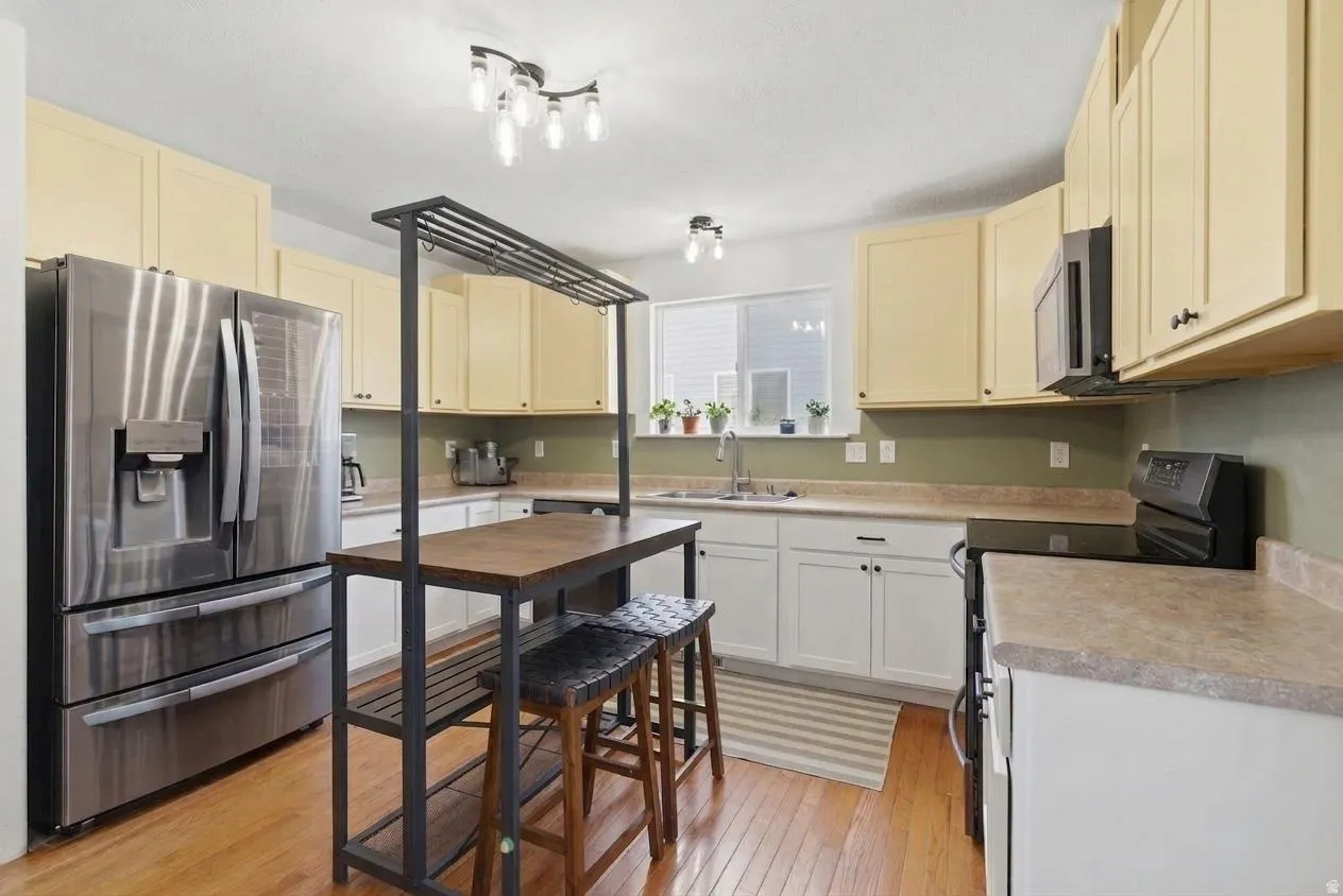 Kitchen featuring wood-finish flooring, two-tone cabinetry, stainless steel refrigerator, built-in microwave, and an undermount sink