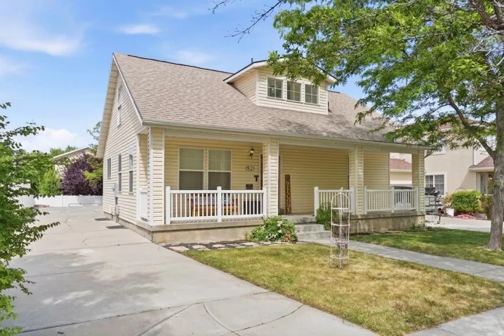 Charming residence featuring a welcoming covered front porch with white railings, light-colored siding, and a gabled roofline