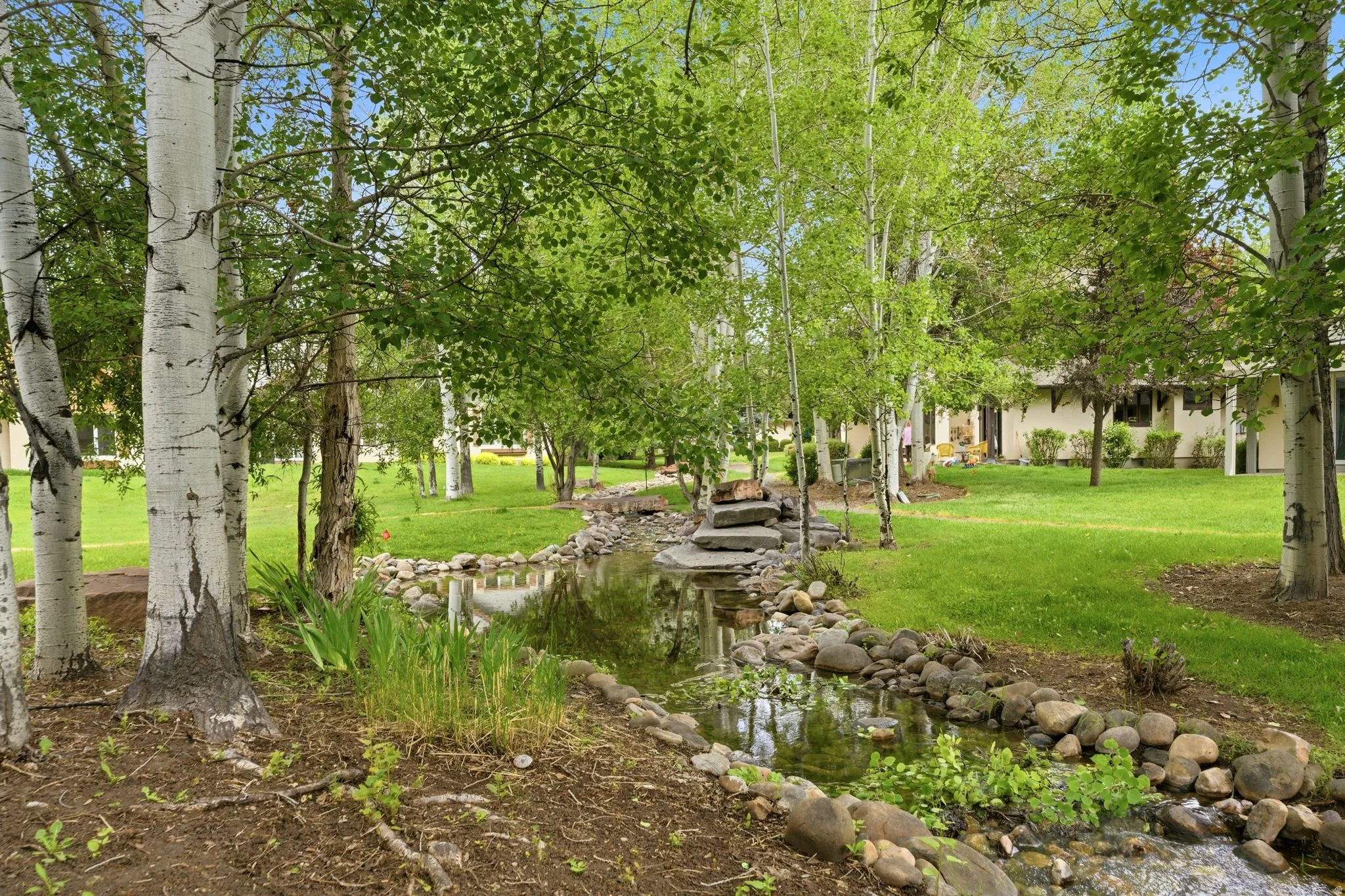 Lush outdoor space featuring a serene rock-lined water feature, mature trees, and expansive green lawns