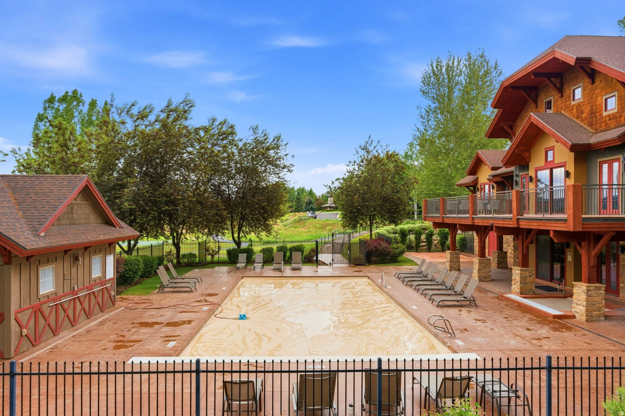 Outdoor swimming pool with a surrounding hardscape patio, bordered by a black metal fence