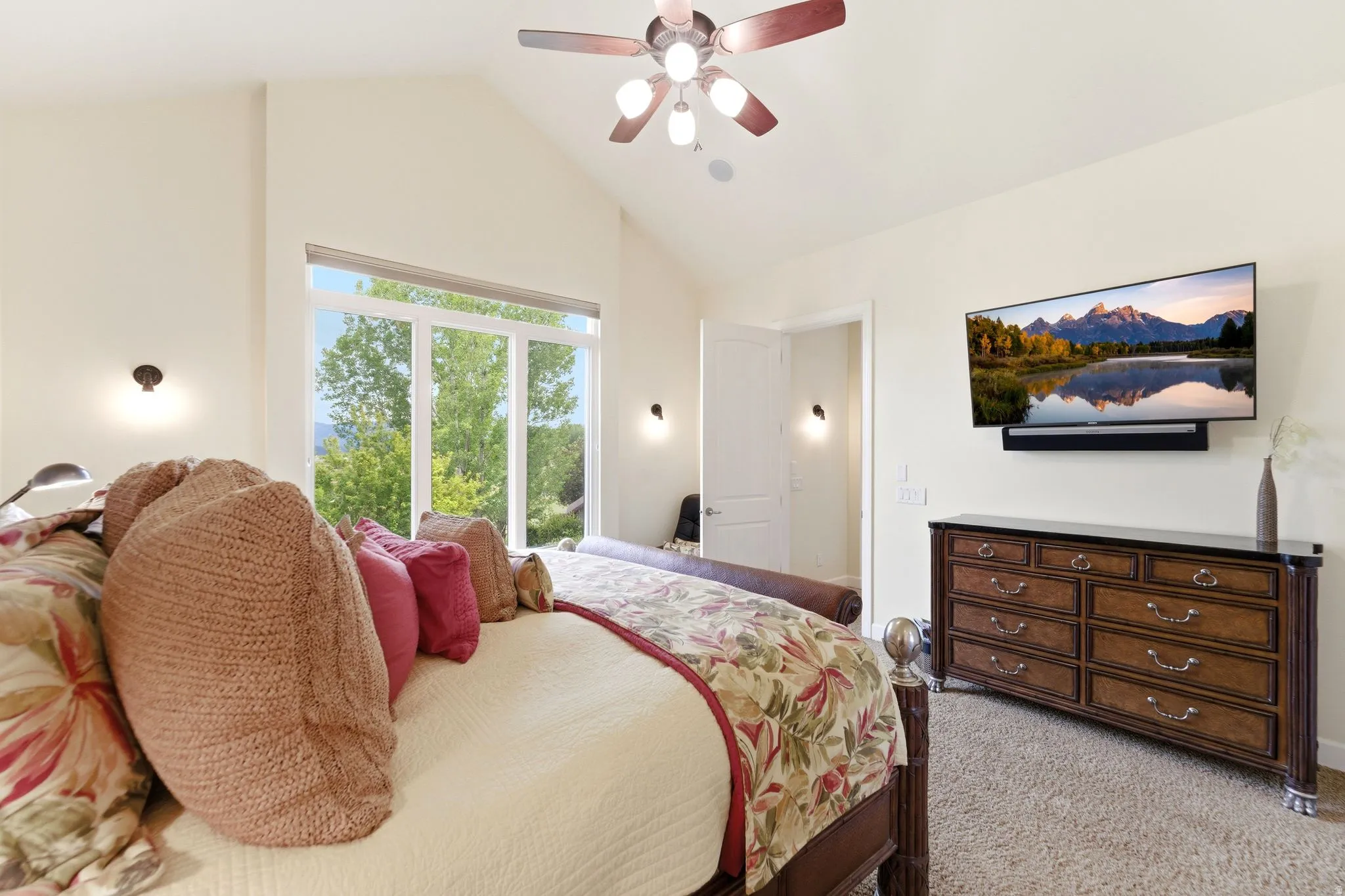 Vaulted ceiling bedroom with a large picture window, a ceiling fan, and two wall-mounted light fixtures