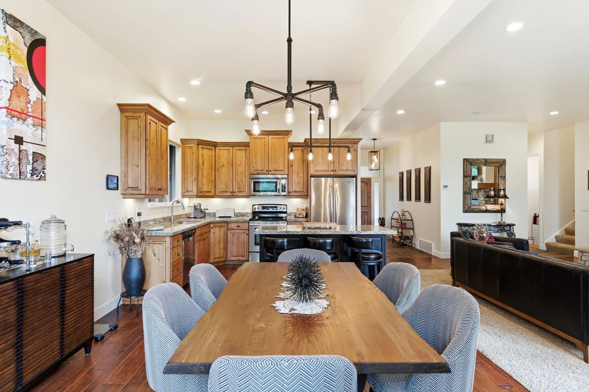 Open-concept living space featuring wood-finish flooring, a kitchen with natural wood cabinetry and stainless steel appliances, a central island with bar seating, and recessed lighting throughout