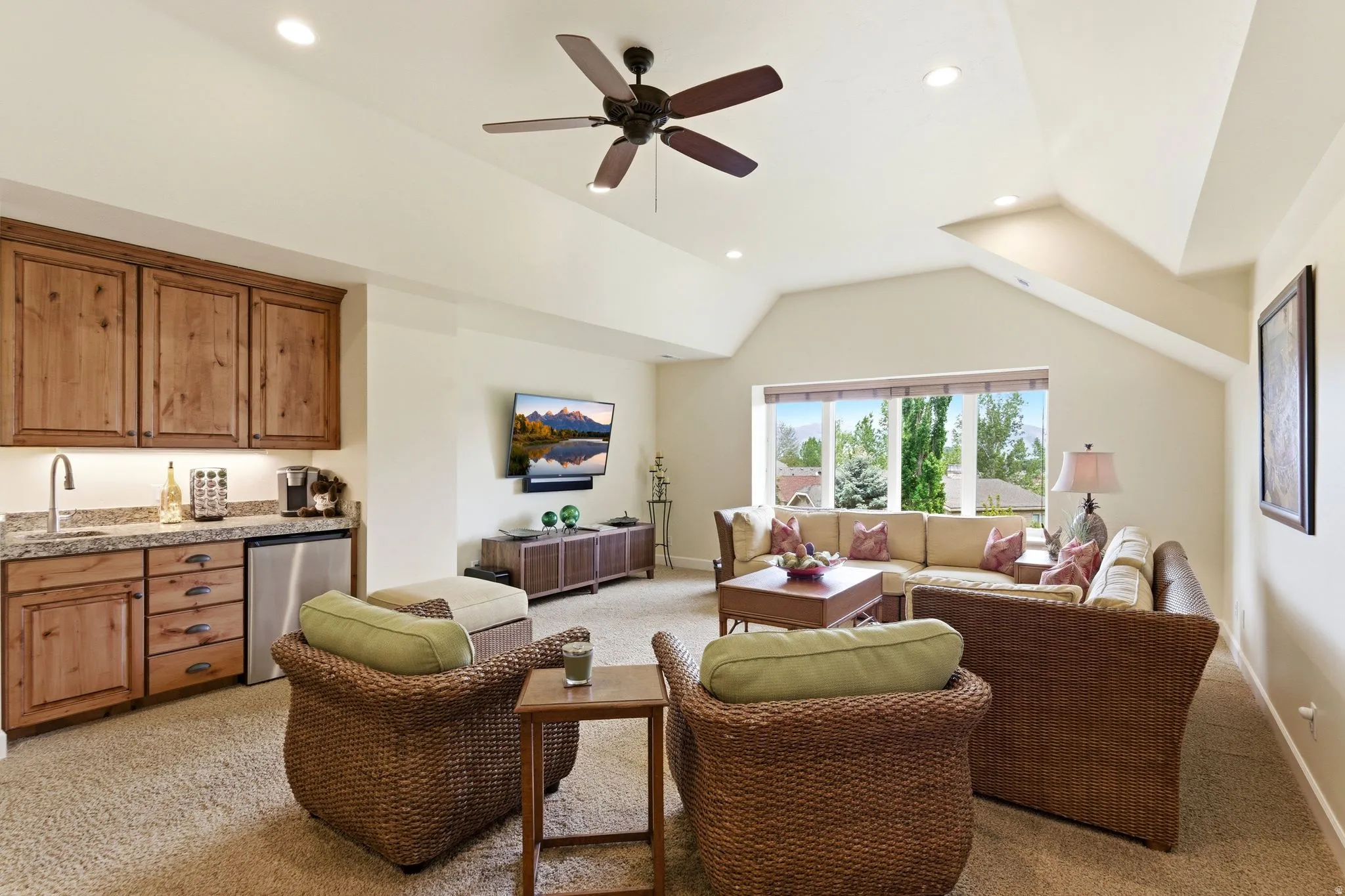 Recessed lighting and a ceiling fan illuminate a spacious room featuring a built-in wet bar with wood cabinetry, a granite-finish countertop, and an undermount sink