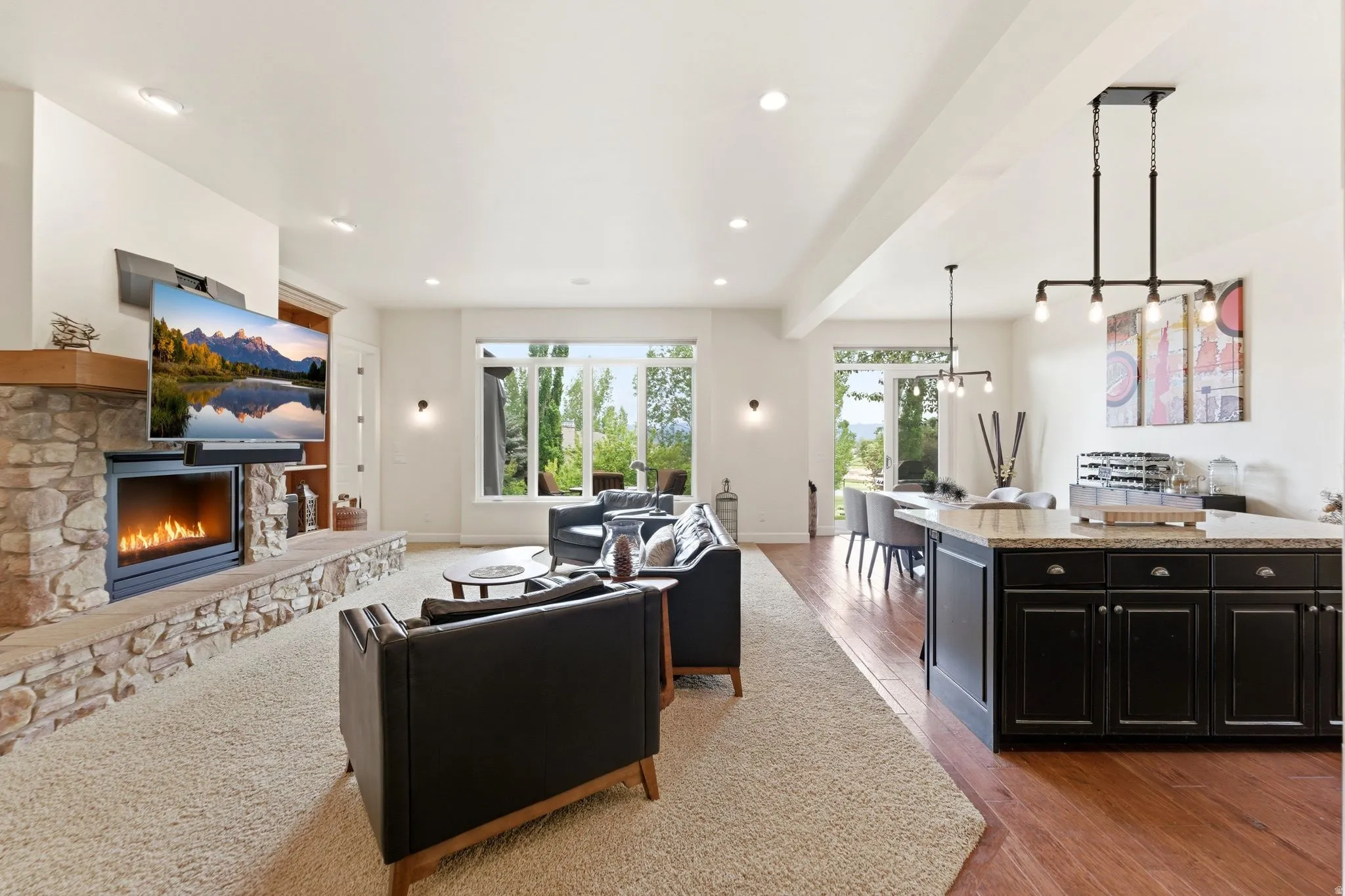Spacious living area featuring a stone fireplace with a wood mantle, large windows, recessed lighting, and mixed flooring with carpet and wood-finish
