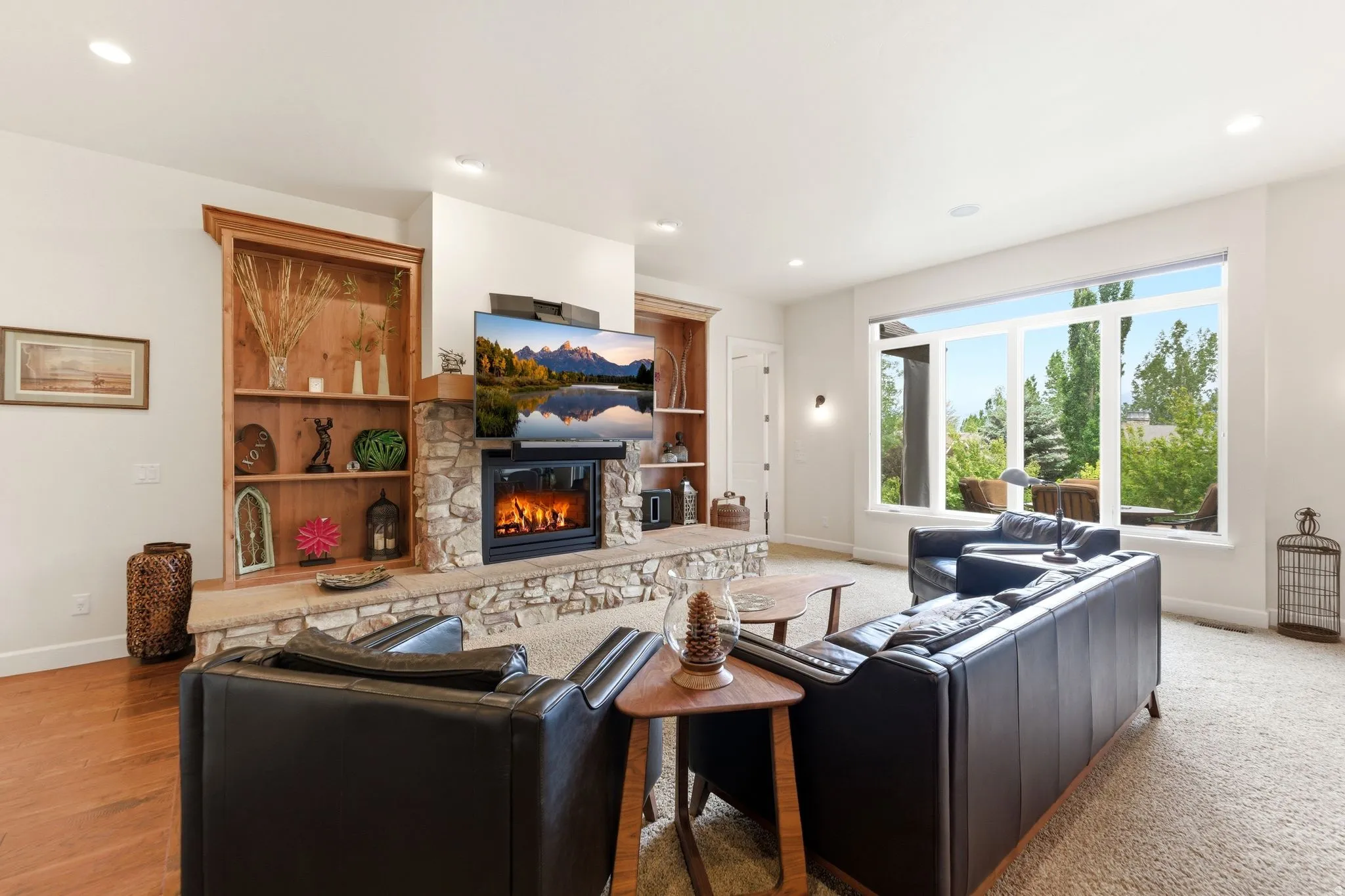Living area featuring a stone-clad fireplace with a wood mantel, built-in timber shelving, a large picture window, recessed lighting, and wood-finish flooring