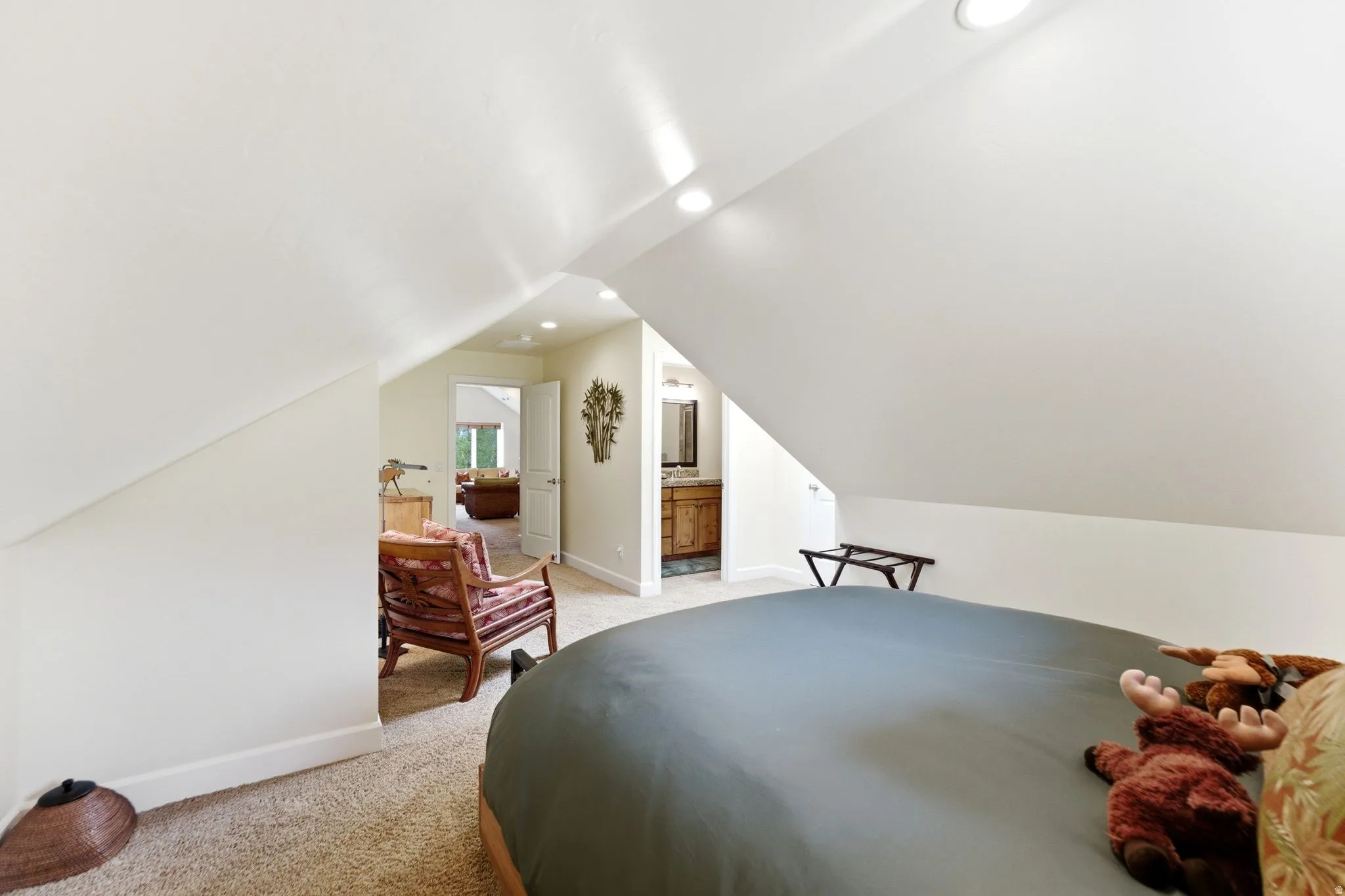 Carpeted attic space featuring sloped ceilings, recessed lighting, and a doorway opening to an additional room