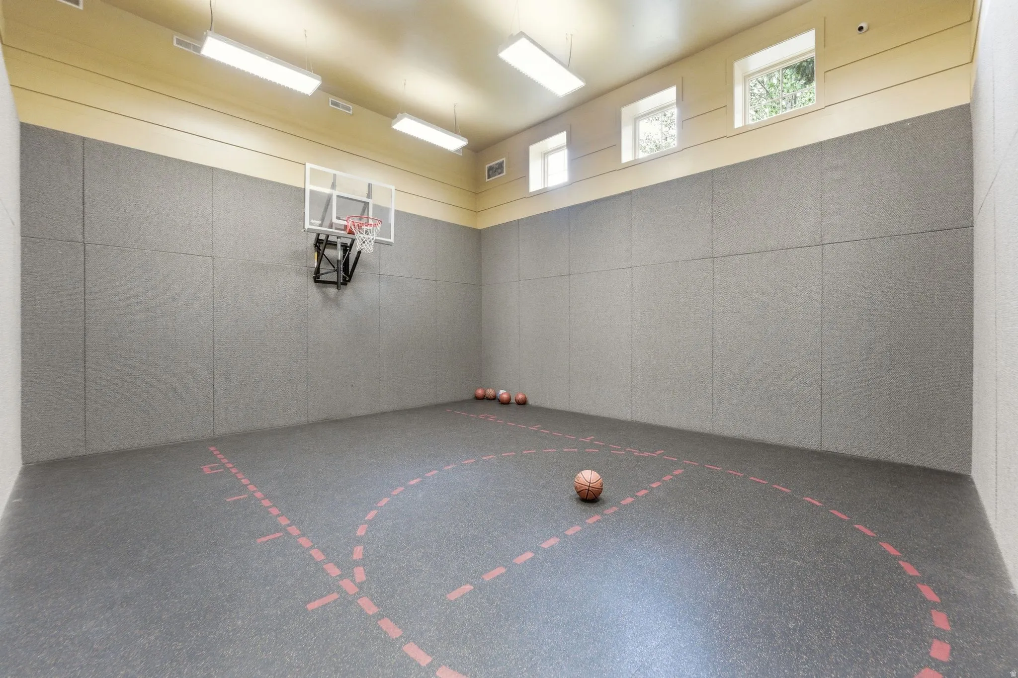 Indoor sports court featuring a basketball hoop, cushioned wall panels, and a marked court surface