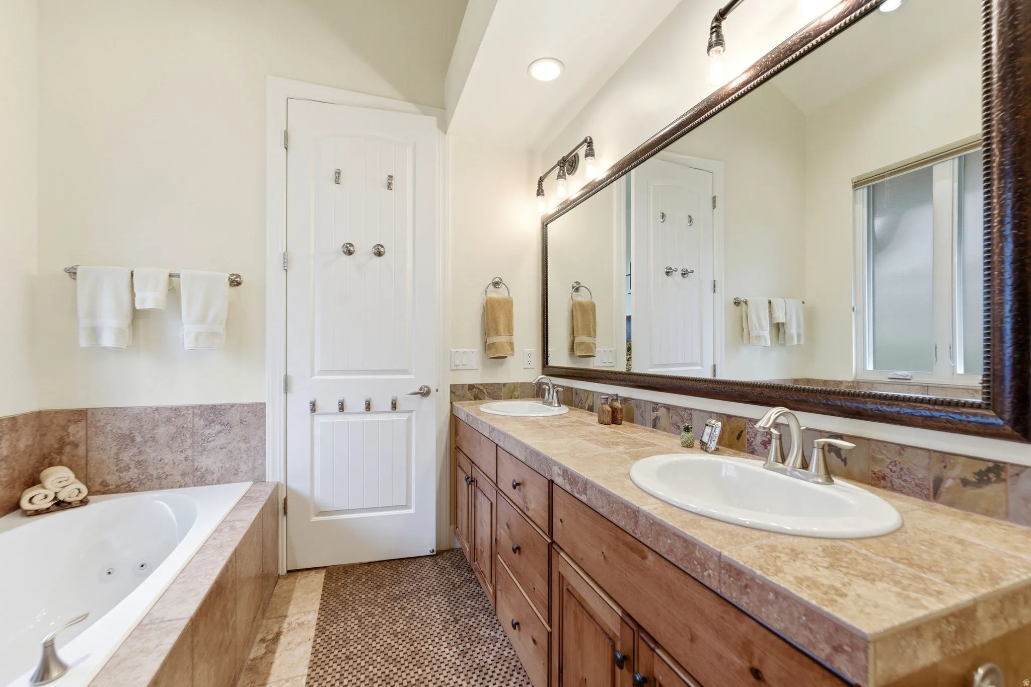 Bathroom featuring a soaking tub, a double vanity with integrated sinks, wood cabinetry, and a large framed mirror