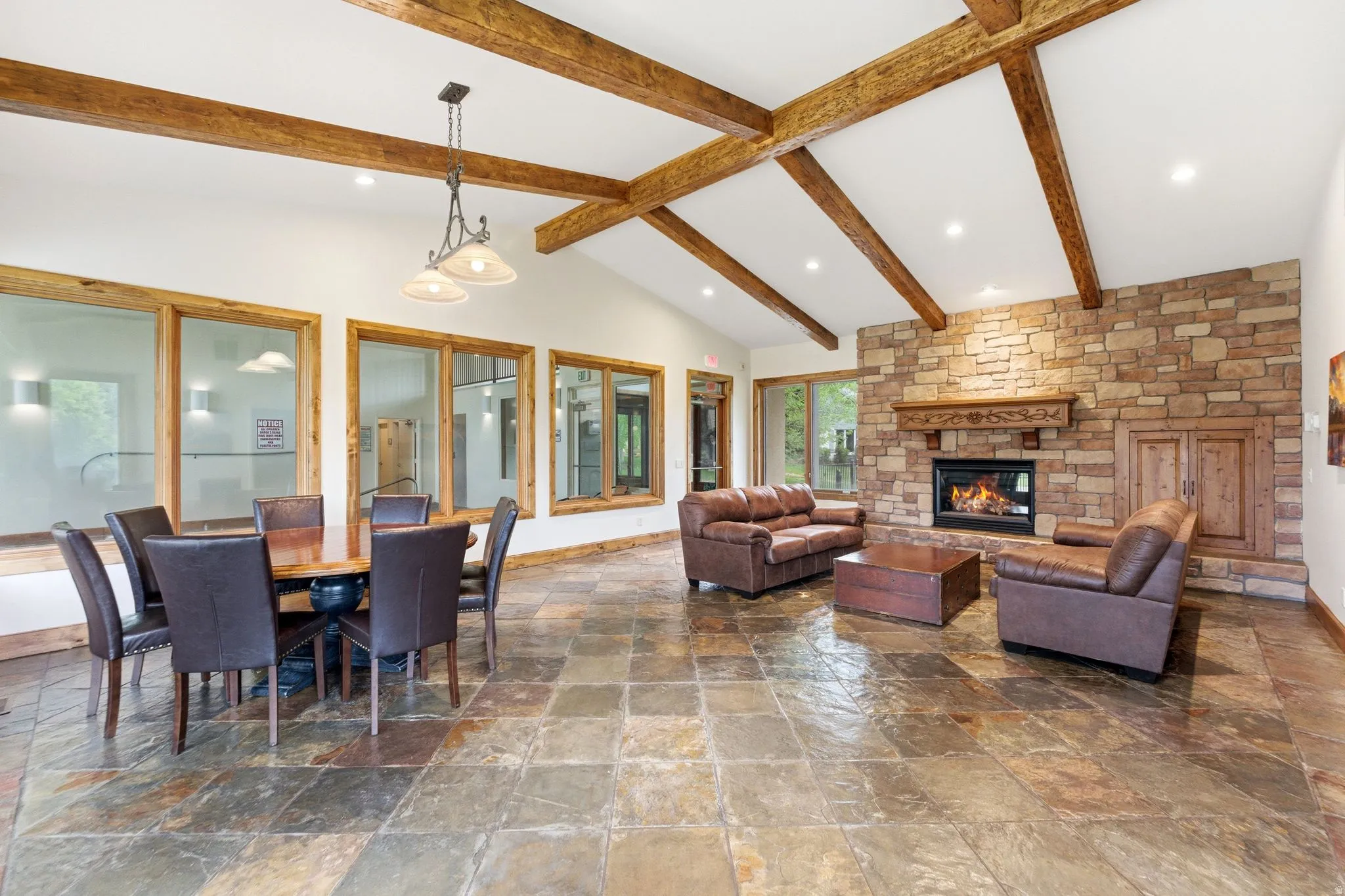 2nd clubhouse Spacious room featuring vaulted ceilings with exposed wood beams, a stone fireplace, and large format stone flooring
