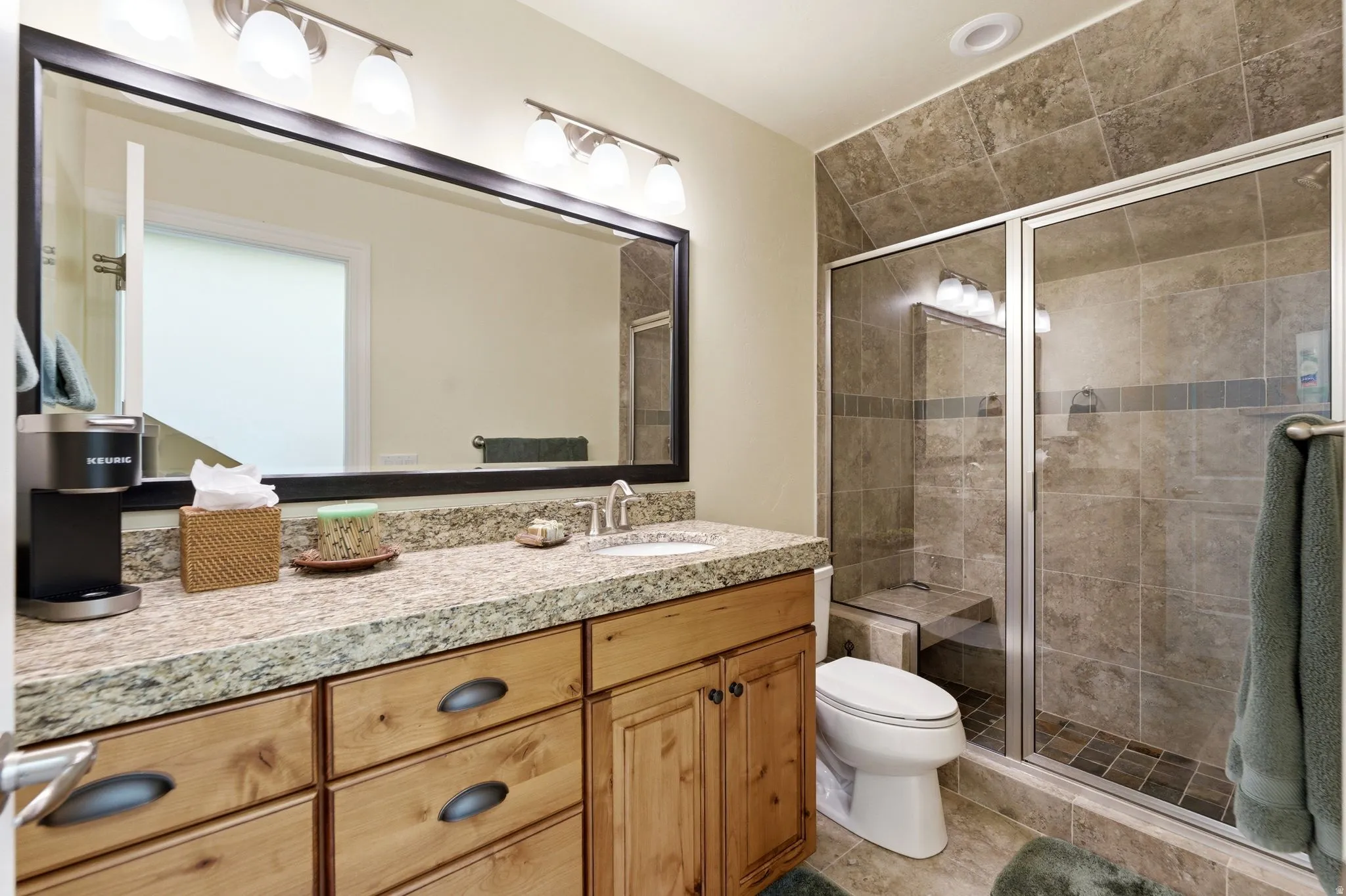 Bathroom featuring a wood-finish vanity with a light-toned countertop, an integrated sink, and a large framed mirror