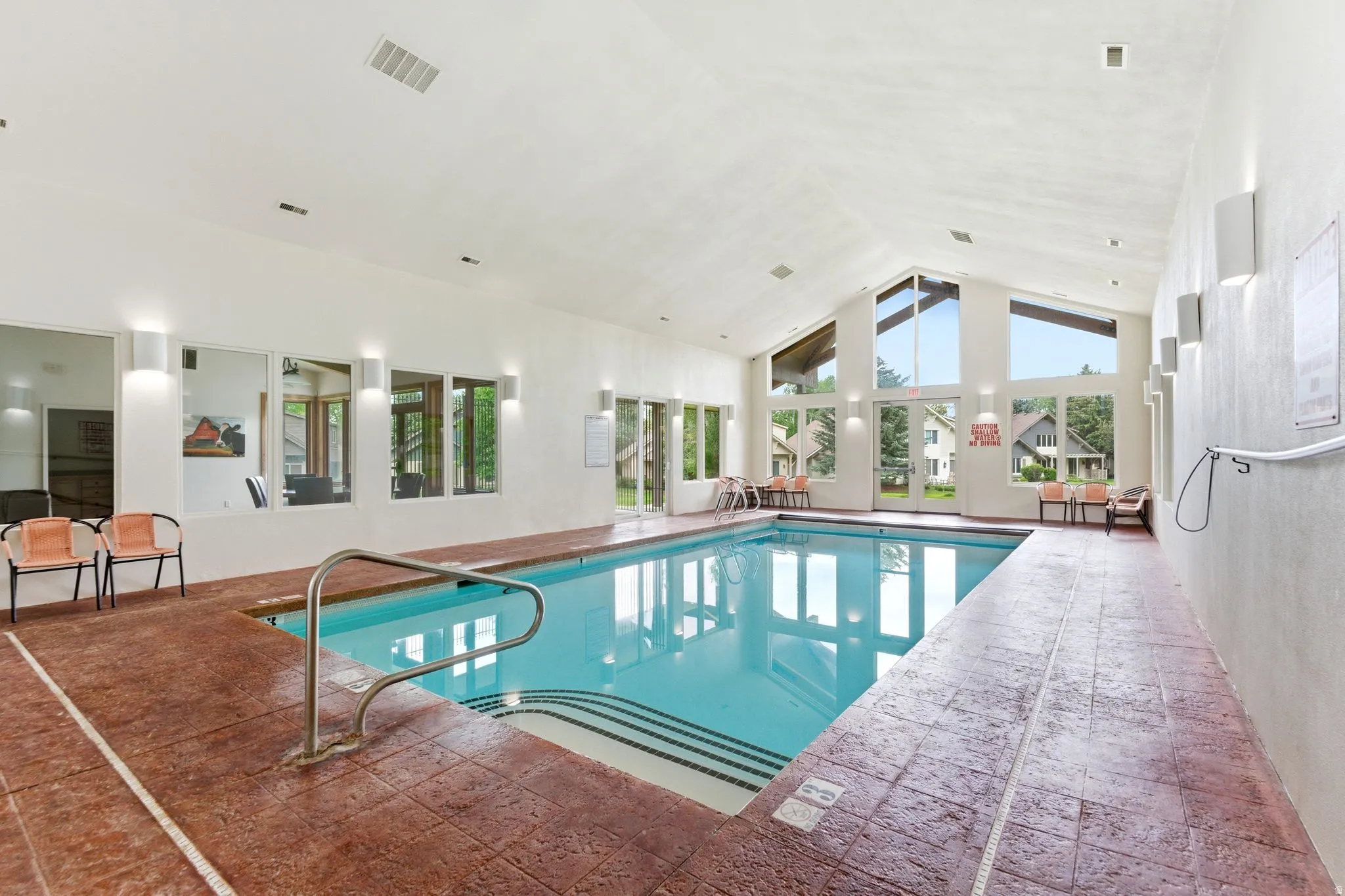 Indoor swimming pool featuring a vaulted ceiling with exposed beams, expansive windows, stamped concrete decking, and multiple wall sconces