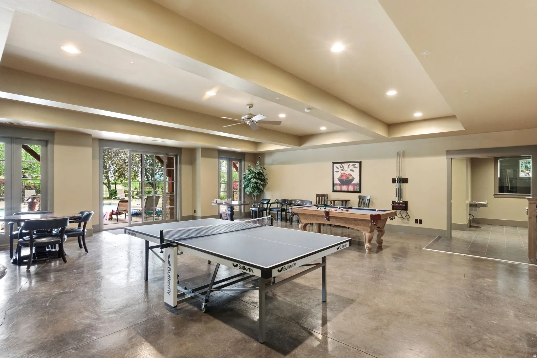 Spacious entertainment room featuring exposed concrete flooring, recessed ceiling lighting, and multiple large glass sliding doors providing abundant natural light