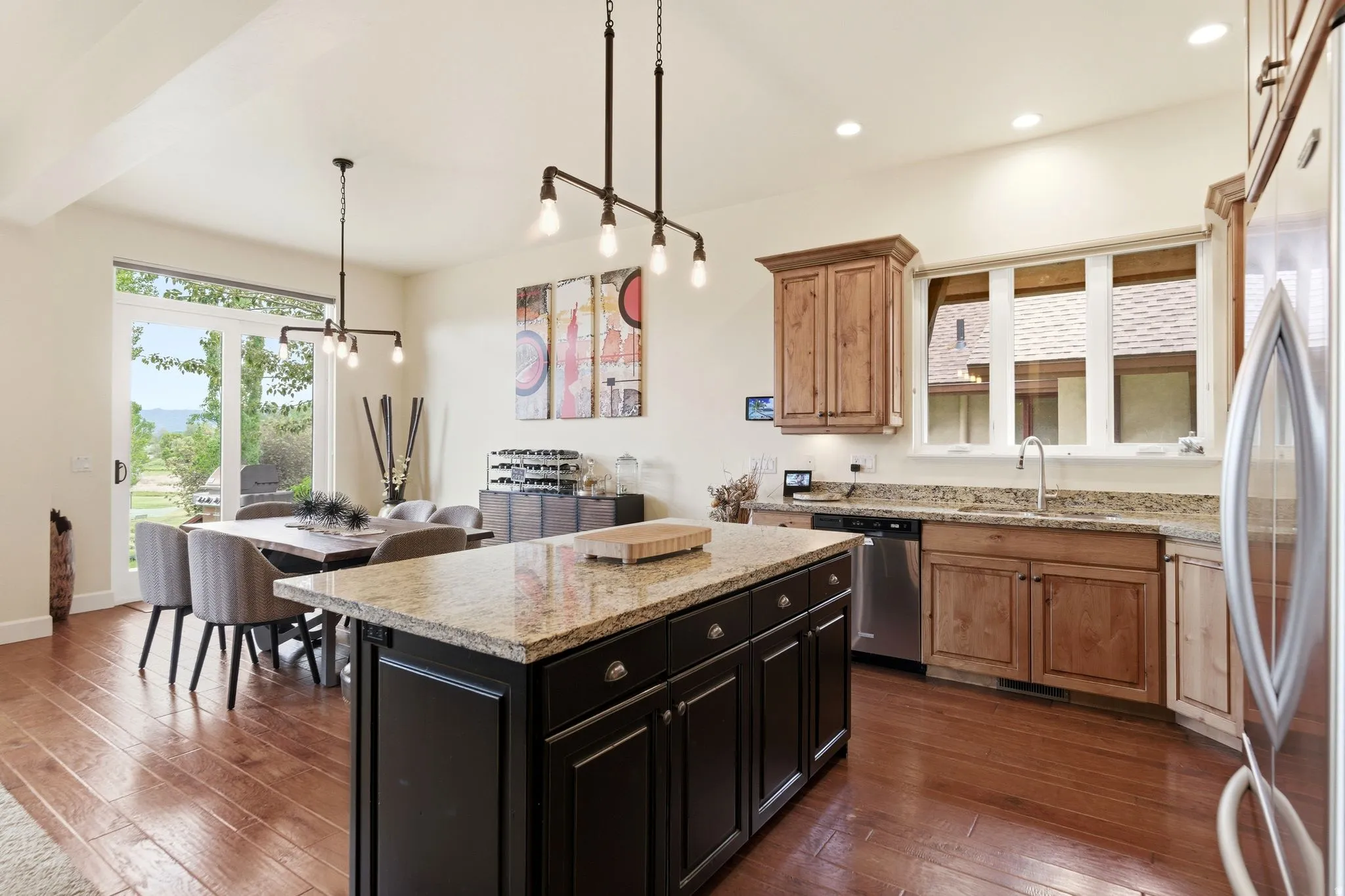 Open-concept kitchen and dining area featuring wood-finish flooring, a dark kitchen island with a light-toned countertop, a kitchen perimeter with wood cabinetry and a light-toned countertop, and a dining area with a glass slider