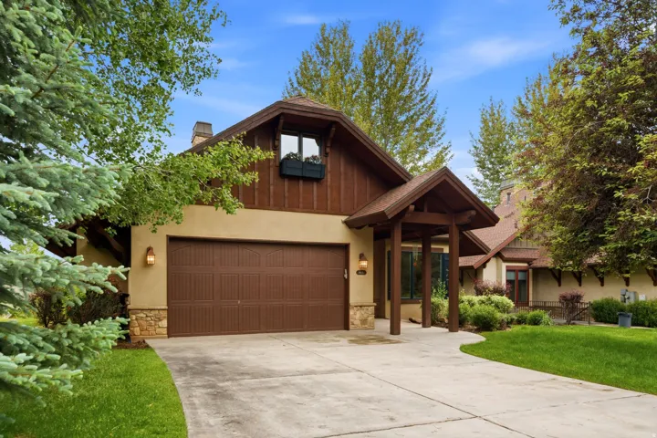 Stucco and wood-paneled exterior with stone accents, featuring an attached garage with a panel door, a covered entry, and a paved driveway