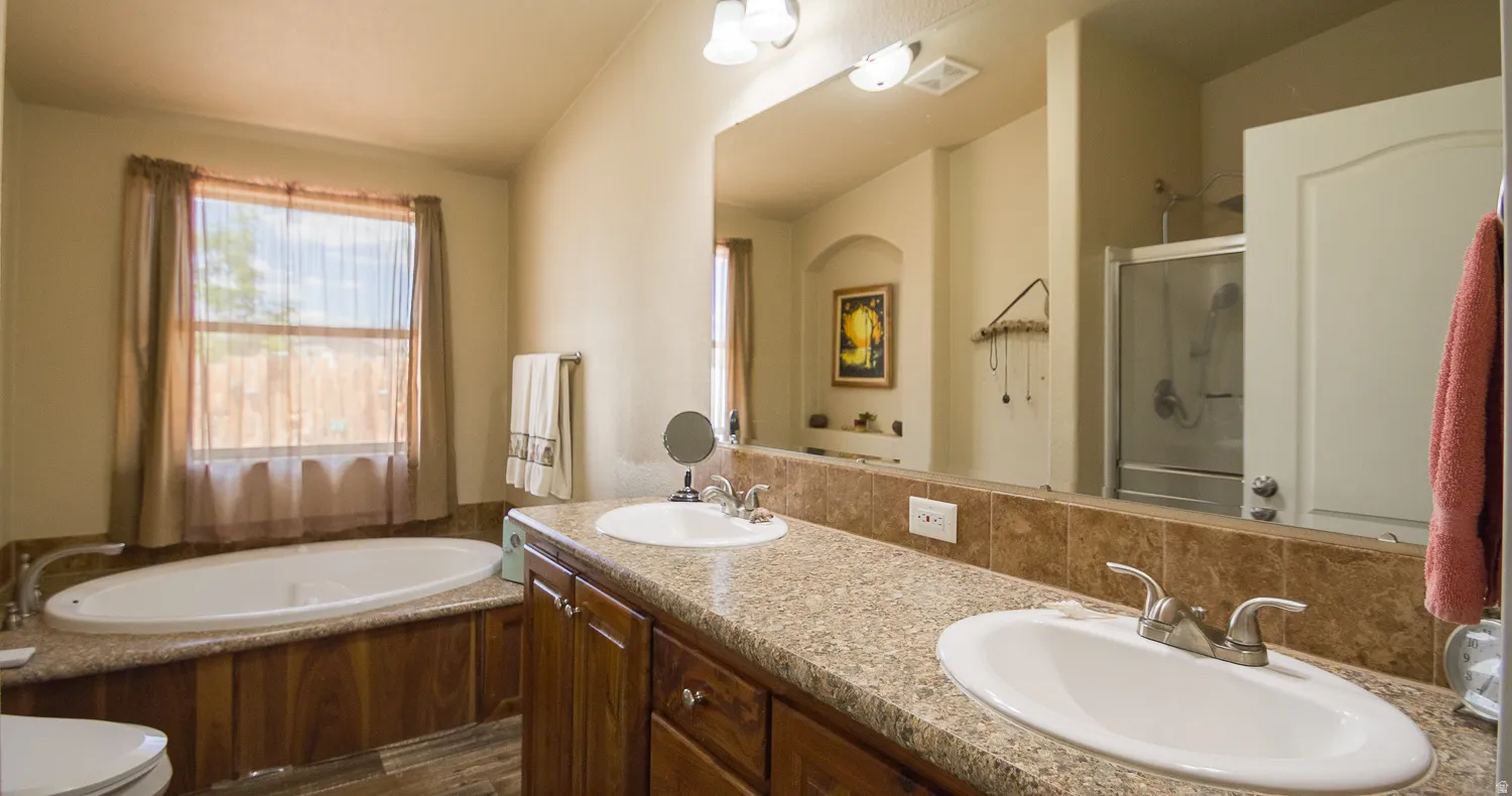 Bathroom featuring dual vanity sinks, a built-in soaking tub, a separate glass-enclosed shower, wood-finish cabinetry, and a window with natural light