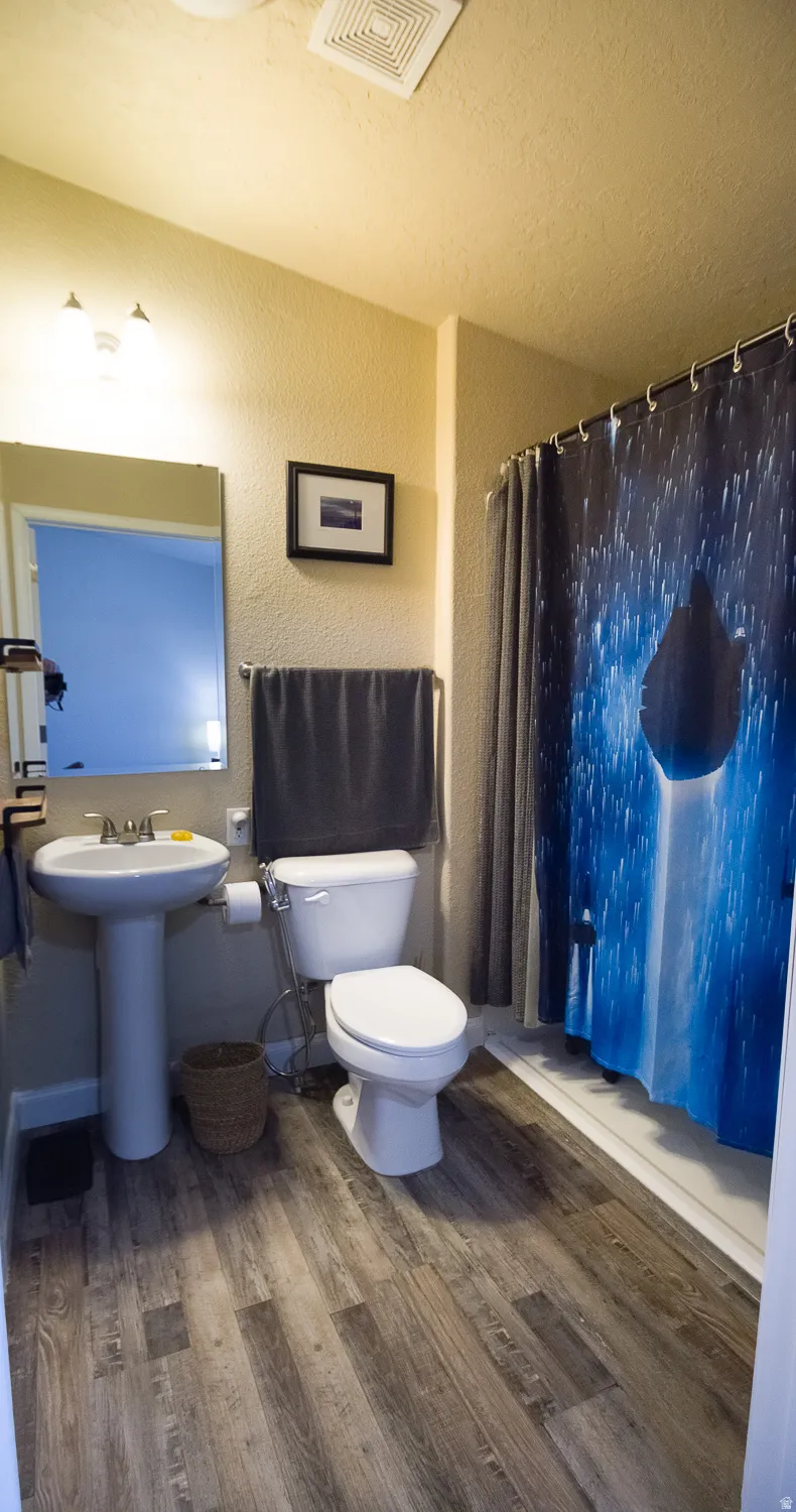 Wood-finish flooring throughout the bathroom, featuring a pedestal sink, a toilet, a shower stall, and an overhead ventilation fan