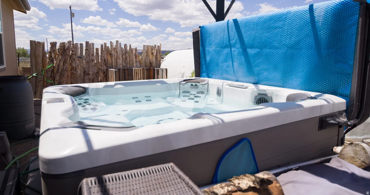 Outdoor spa featuring a light-colored shell, dark-colored exterior paneling, and a natural wood fence backdrop