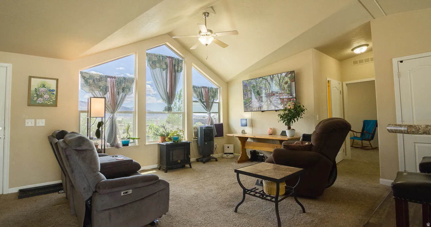 Spacious living area featuring a vaulted ceiling with a ceiling fan, multiple triangular windows, and carpeted flooring