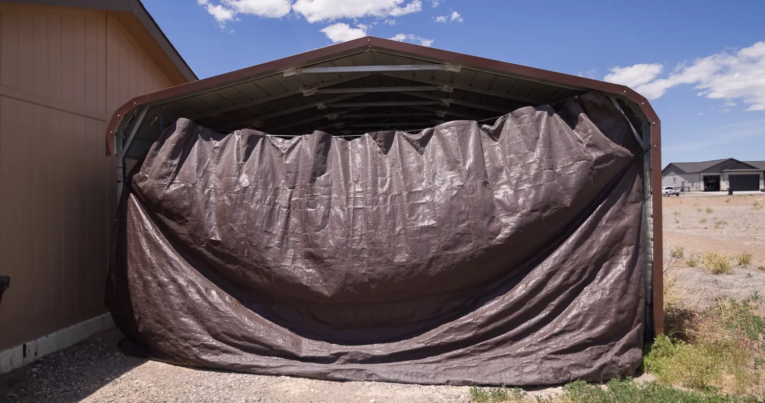 Freestanding metal carport structure featuring a brown tarp enclosure