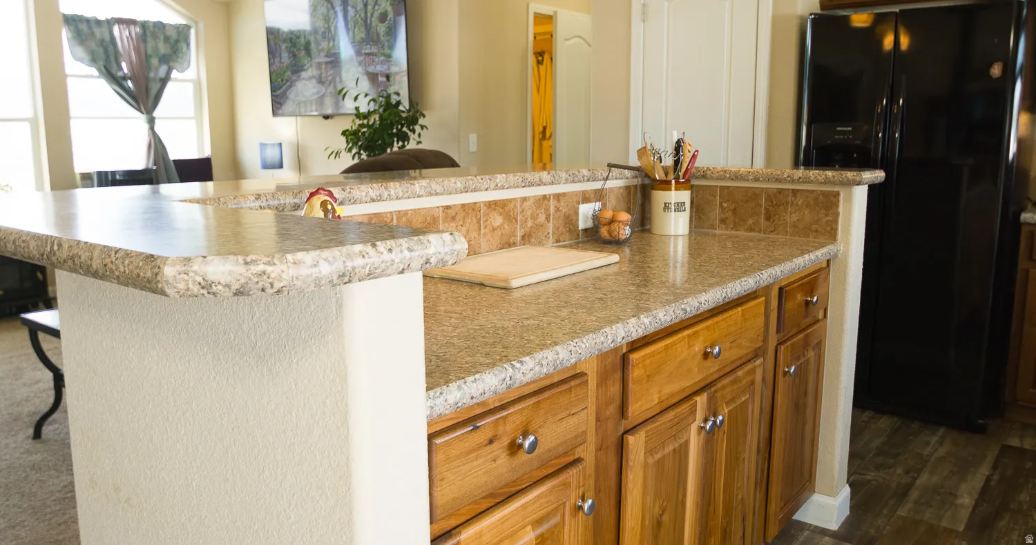 Kitchen island featuring granite-look countertops, wood cabinetry with silver hardware, and a tile backsplash