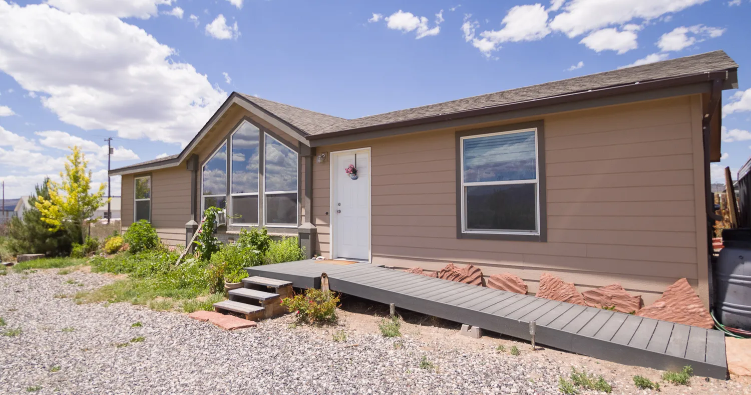 Horizontal siding exterior featuring a prominent gabled window wall, white entry door, and dark grey composite decking with both stairs and ramp access