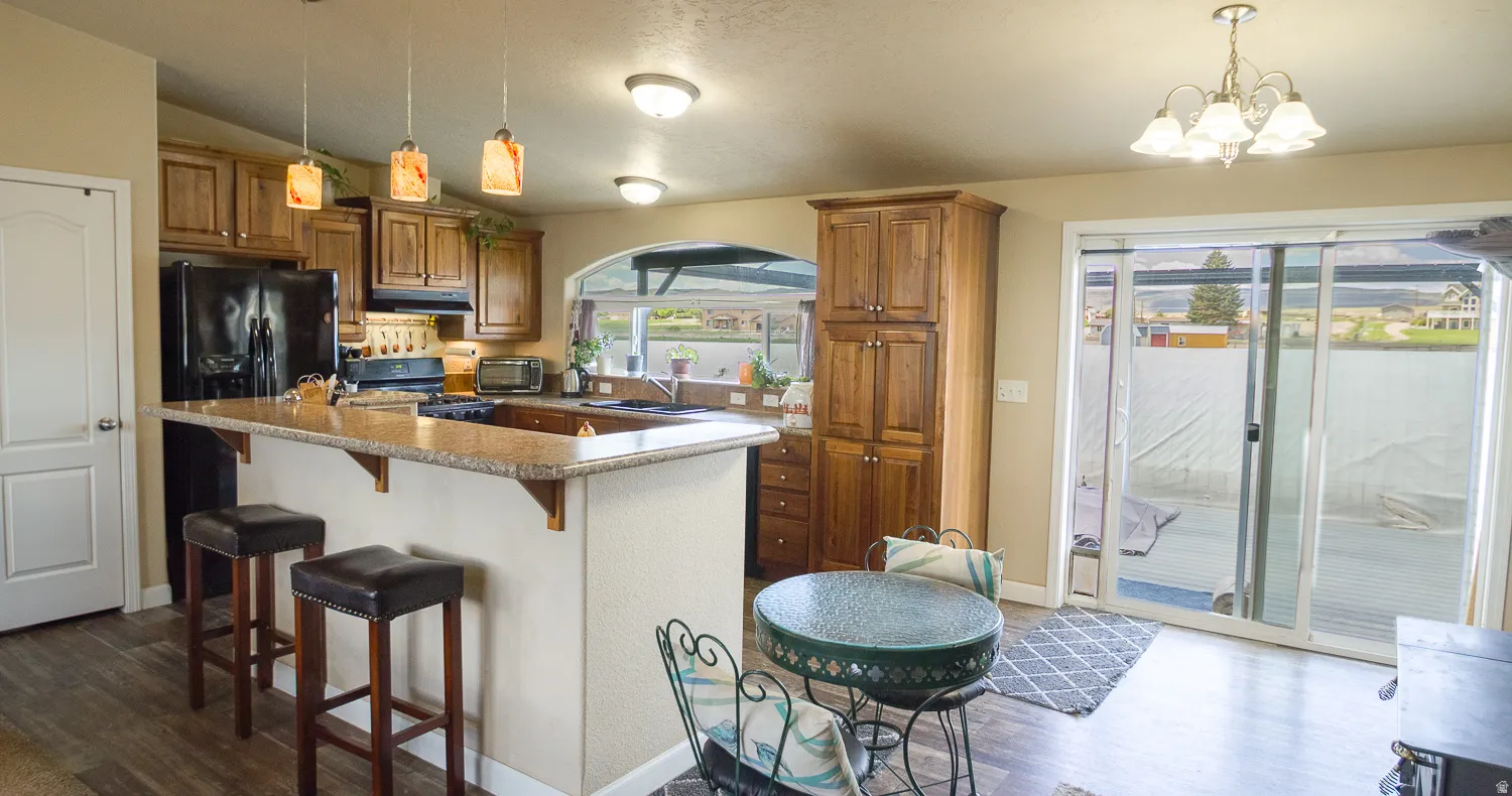 Kitchen featuring wood-finish flooring, wood cabinetry, a breakfast bar with stone-finish countertop, and a black appliance package