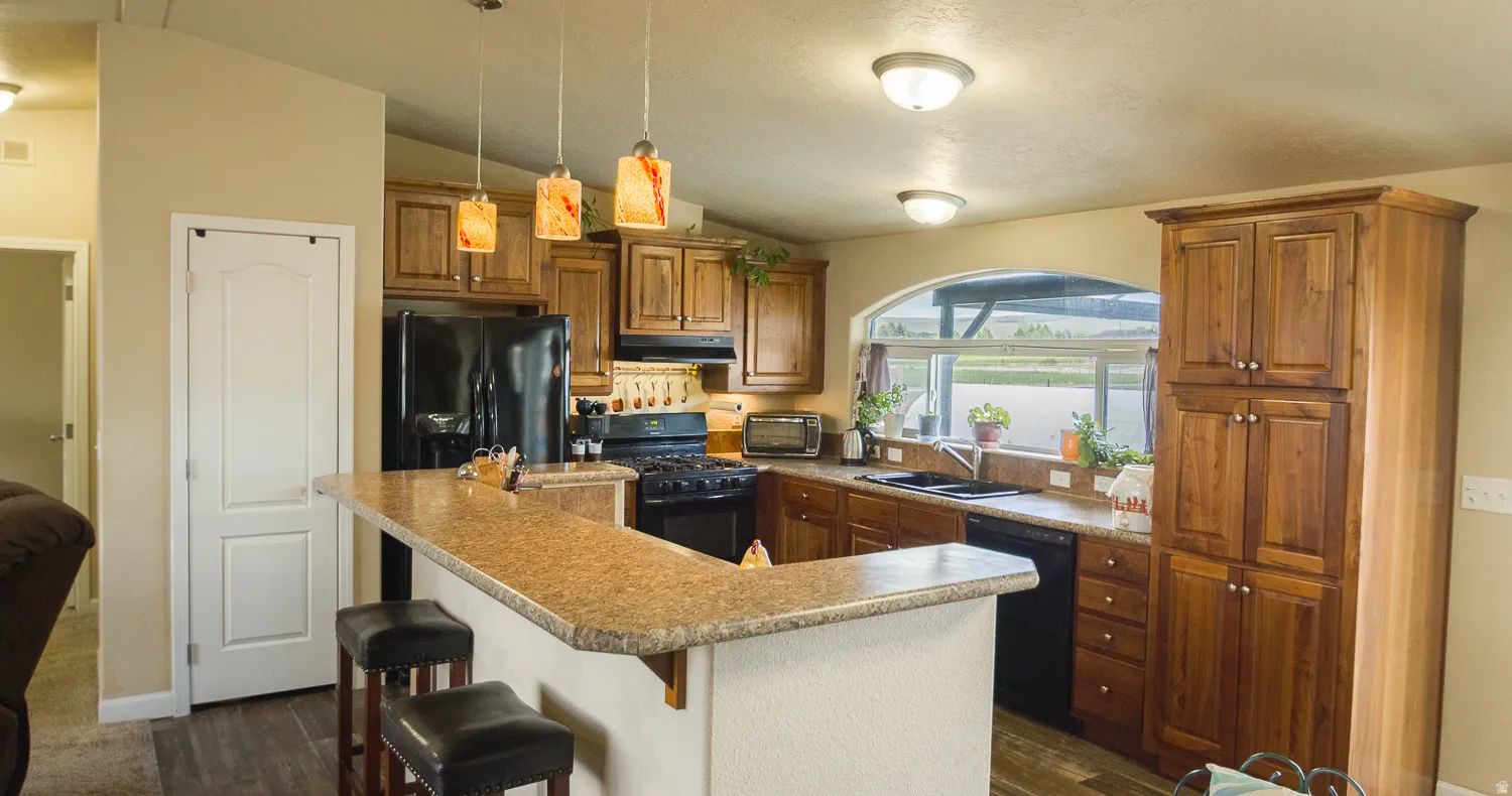 Kitchen with wood-finish cabinetry, black appliances, and a breakfast bar with pendant lighting