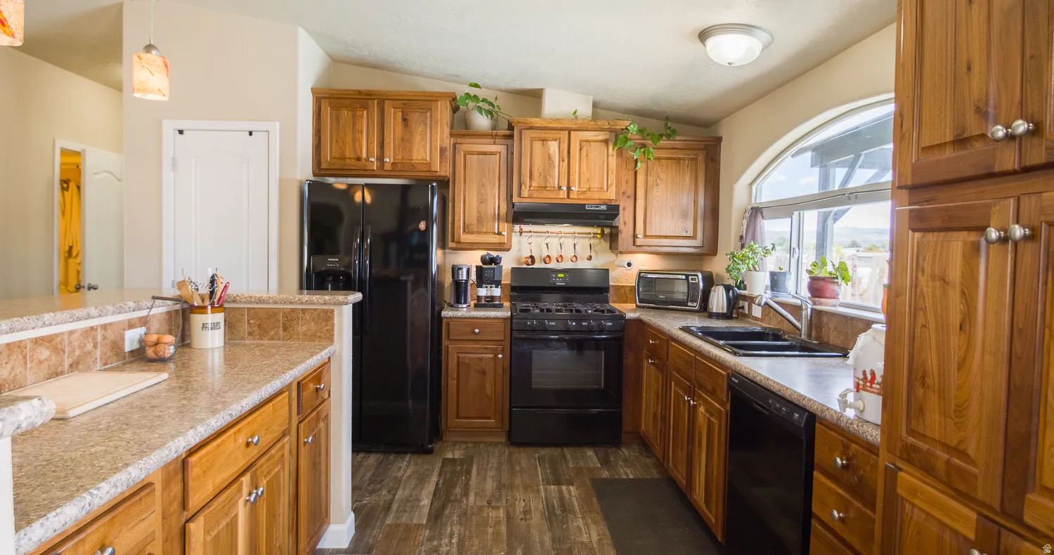 Kitchen featuring wood-finish cabinetry, black appliances, solid surface countertops, and a large arched window