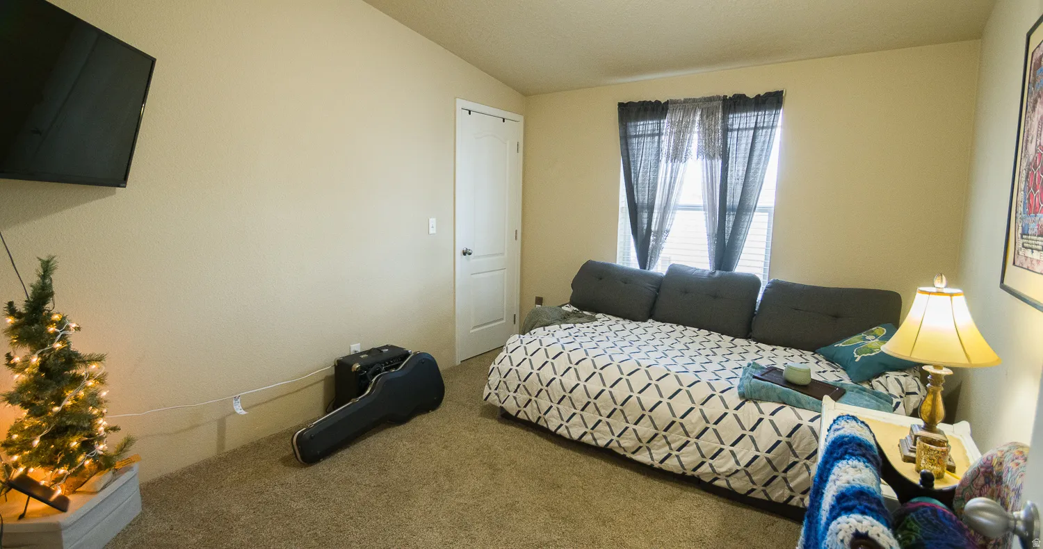 Carpeted room featuring a window with blinds, a wall-mounted television, and a white interior door