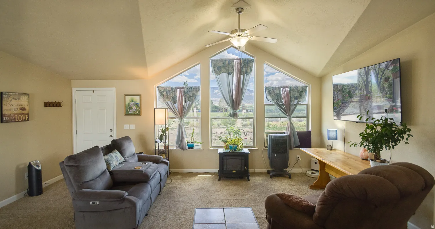 Spacious living area featuring a vaulted ceiling with a ceiling fan, three large trapezoidal windows, and neutral carpeting