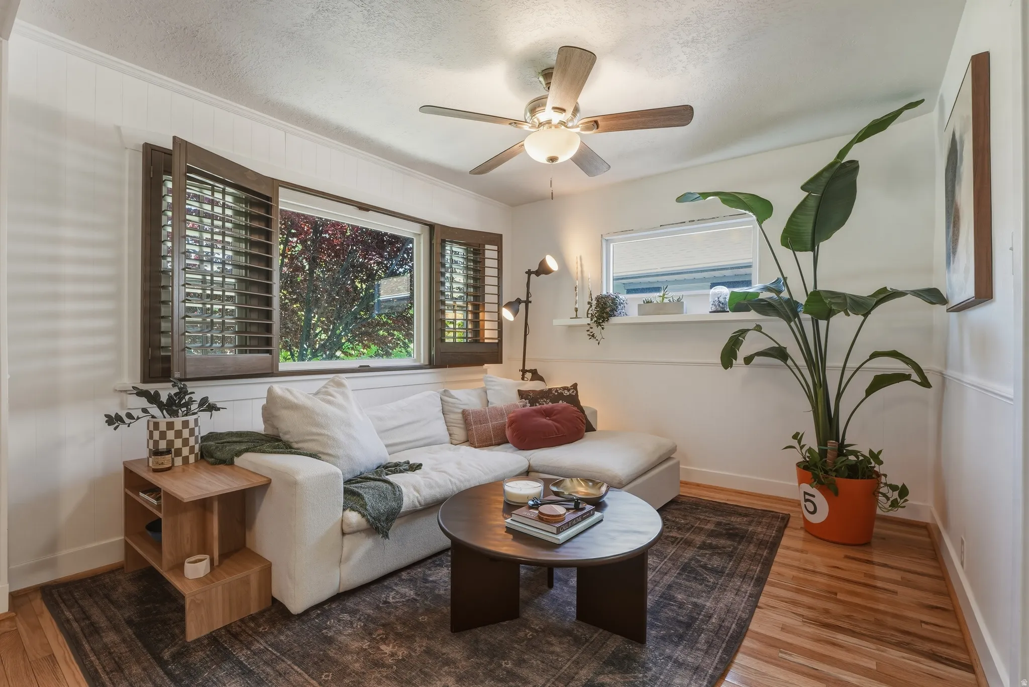 Hardwood flooring extends throughout this space, featuring white paneled walls and a ceiling fan with integrated lighting