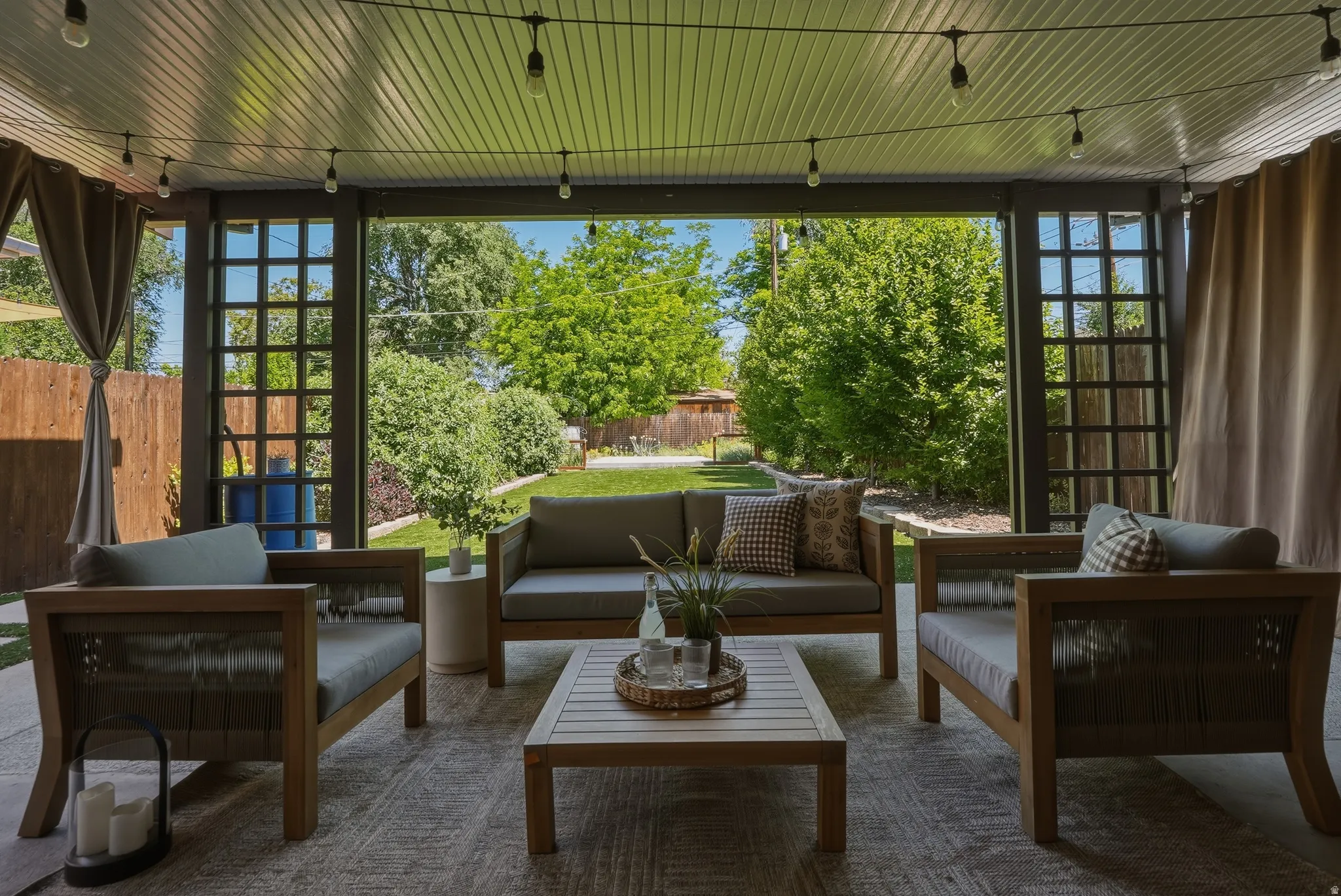 Covered patio featuring a slatted ceiling, string lighting, and privacy curtains