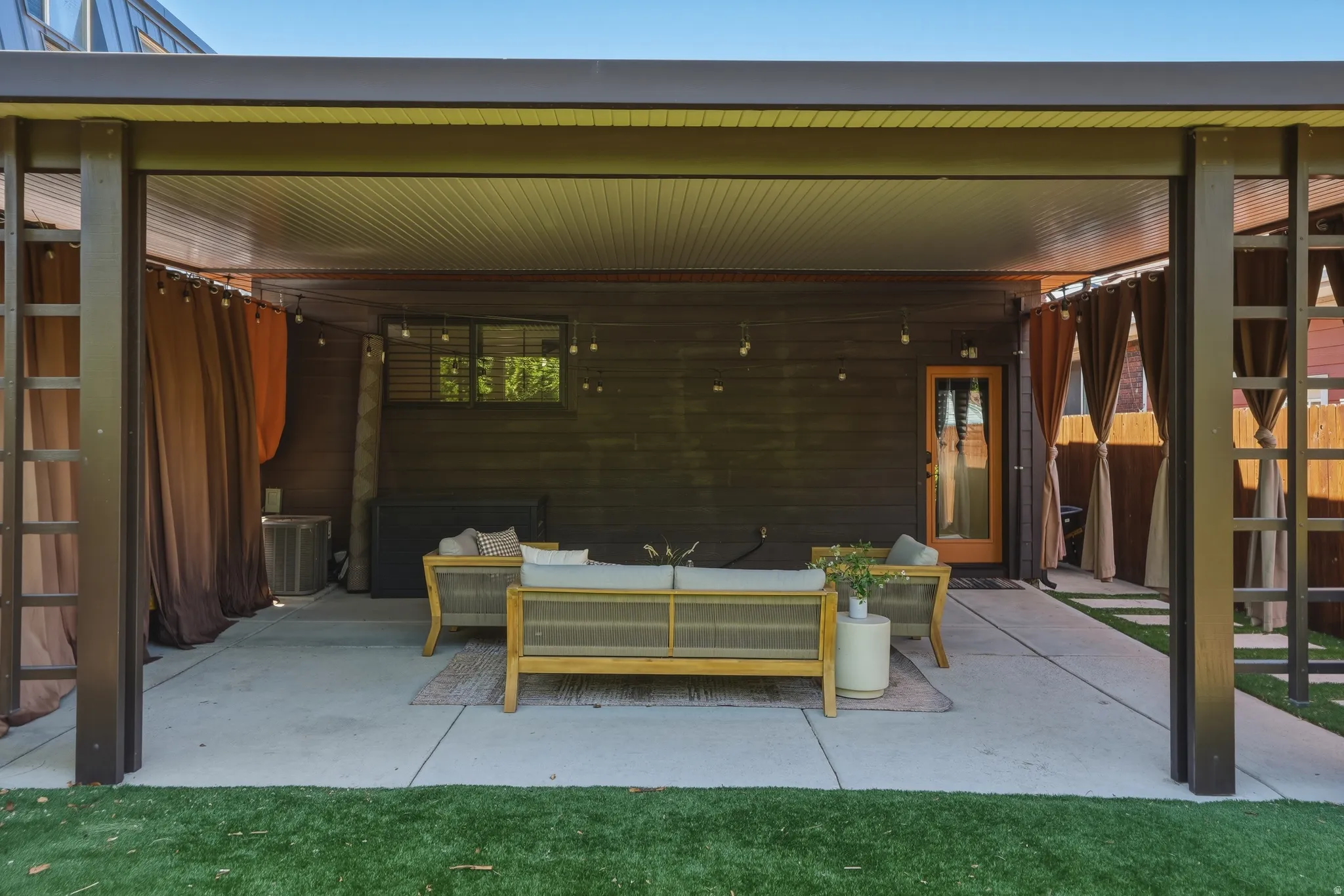 Expansive covered patio featuring a concrete slab, dark wood-paneled exterior wall, and string lighting