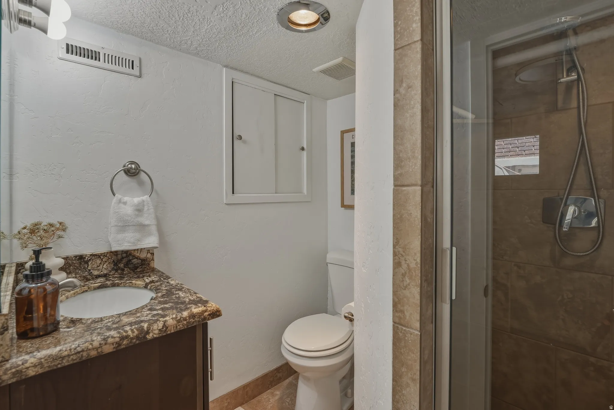 Bathroom featuring a glass-enclosed shower with tile surround, a vanity with a stone-finish countertop, an undermount sink, and a commode