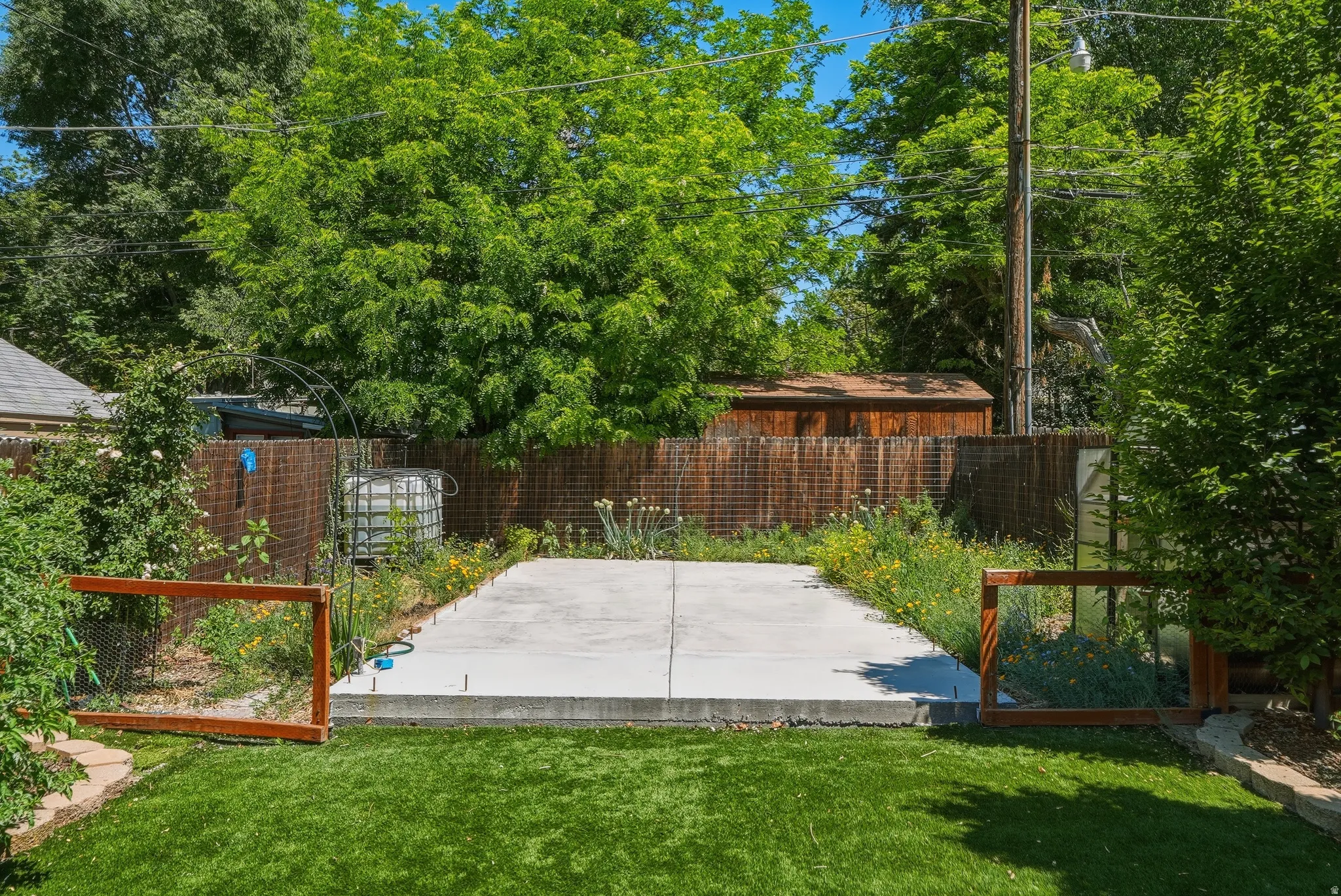 Expansive outdoor space featuring a manicured lawn, concrete pad, wood privacy fencing, and mature trees