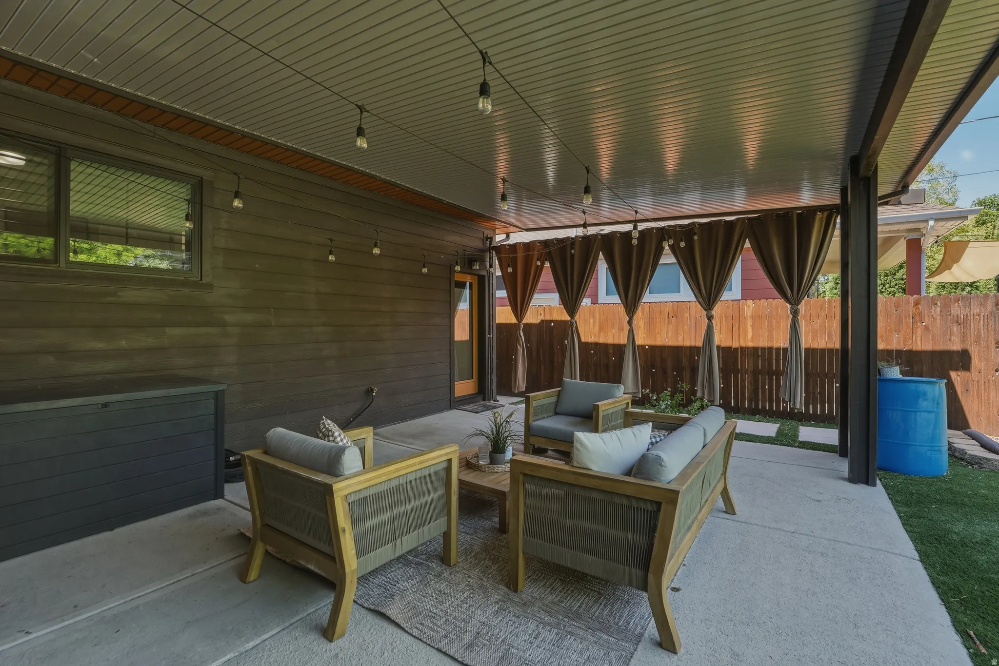 Covered patio featuring a concrete slab, string lighting, privacy curtains, and a wooden fence
