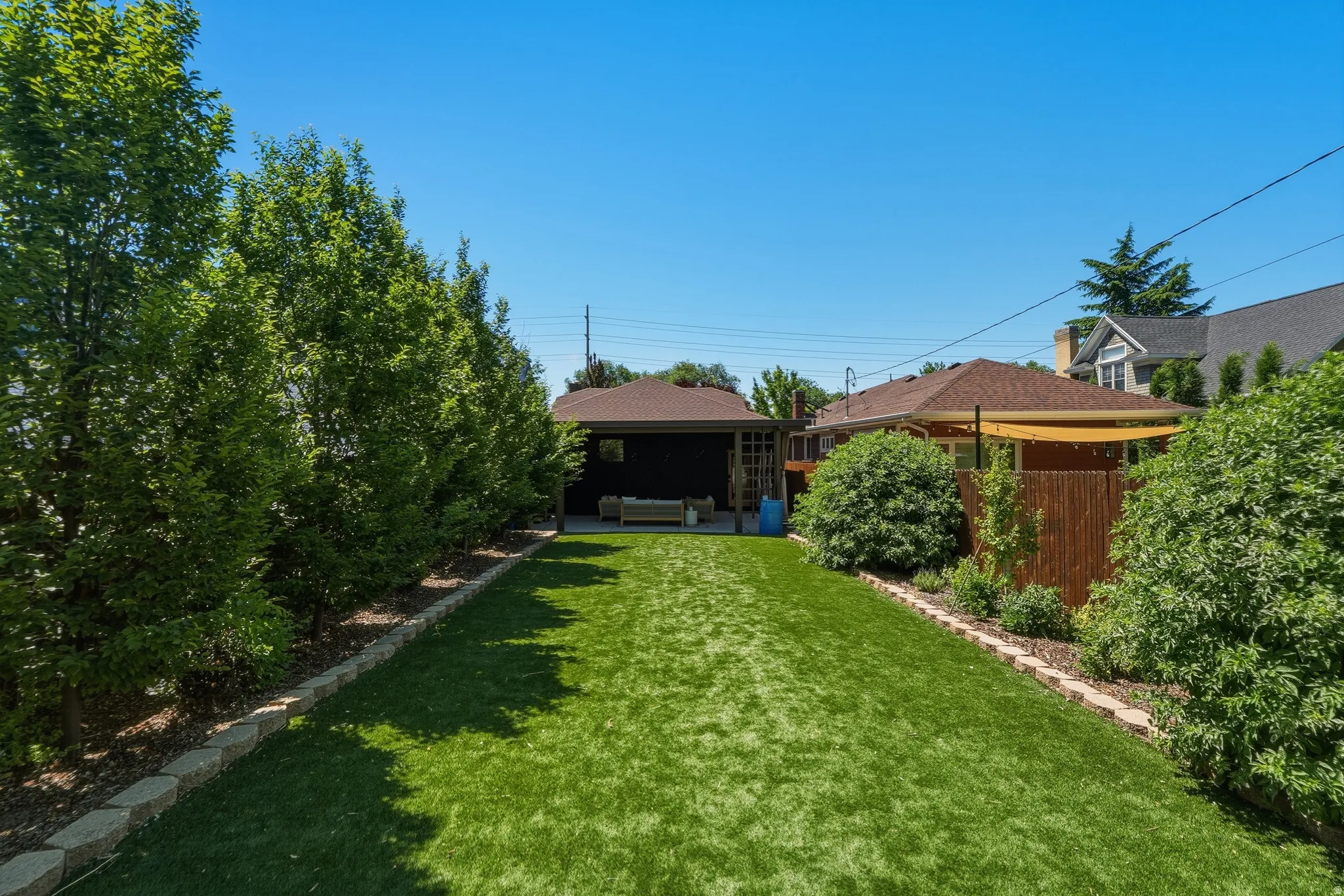 Expansive backyard featuring a manicured lawn, established privacy trees, a retaining wall border, and a wooden fence