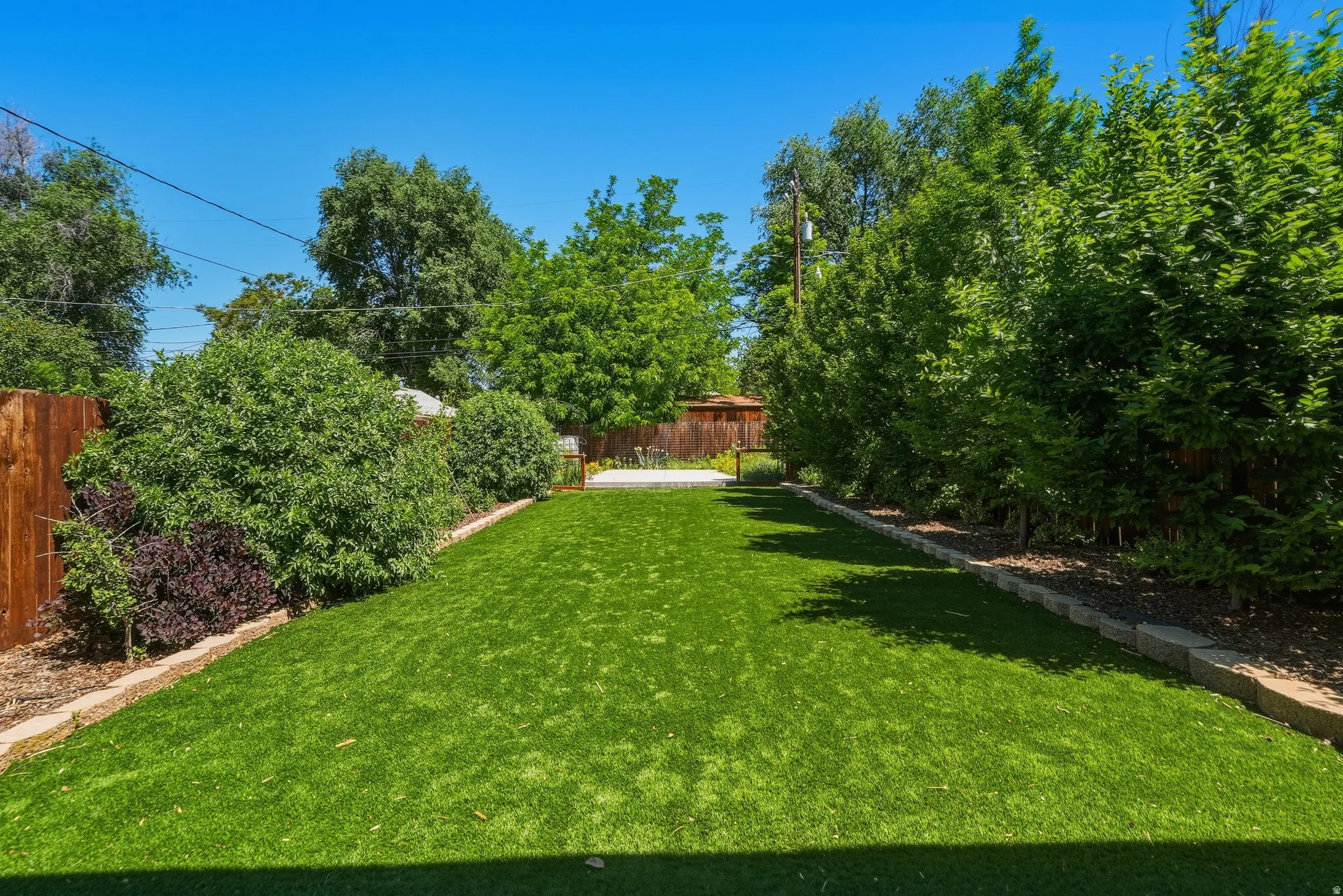 Expansive backyard featuring artificial turf, mature perimeter trees, and a wooden privacy fence