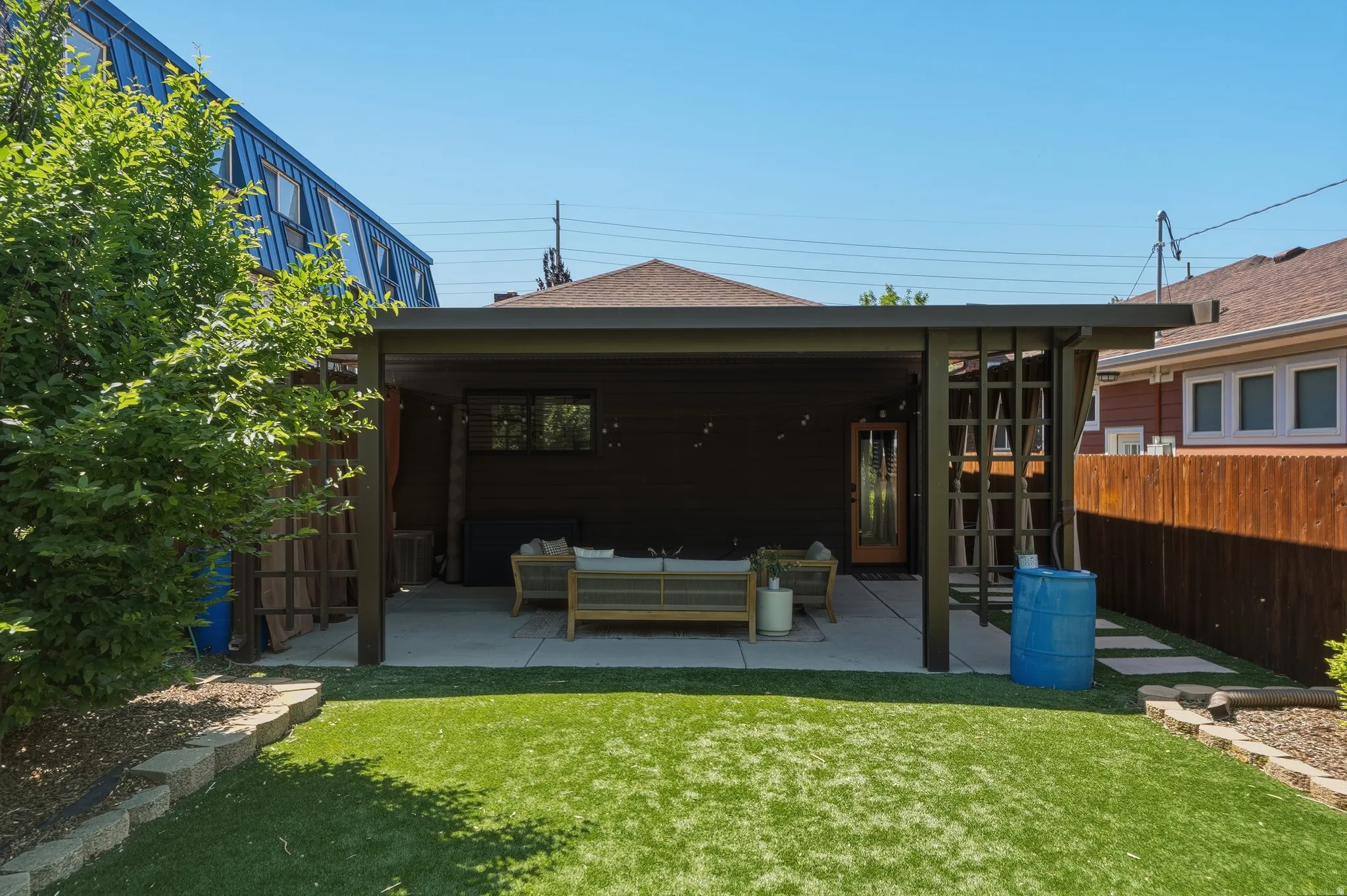 Backyard patio featuring a dark-toned covered structure with string lighting, a concrete surface, and a wood-paneled exterior